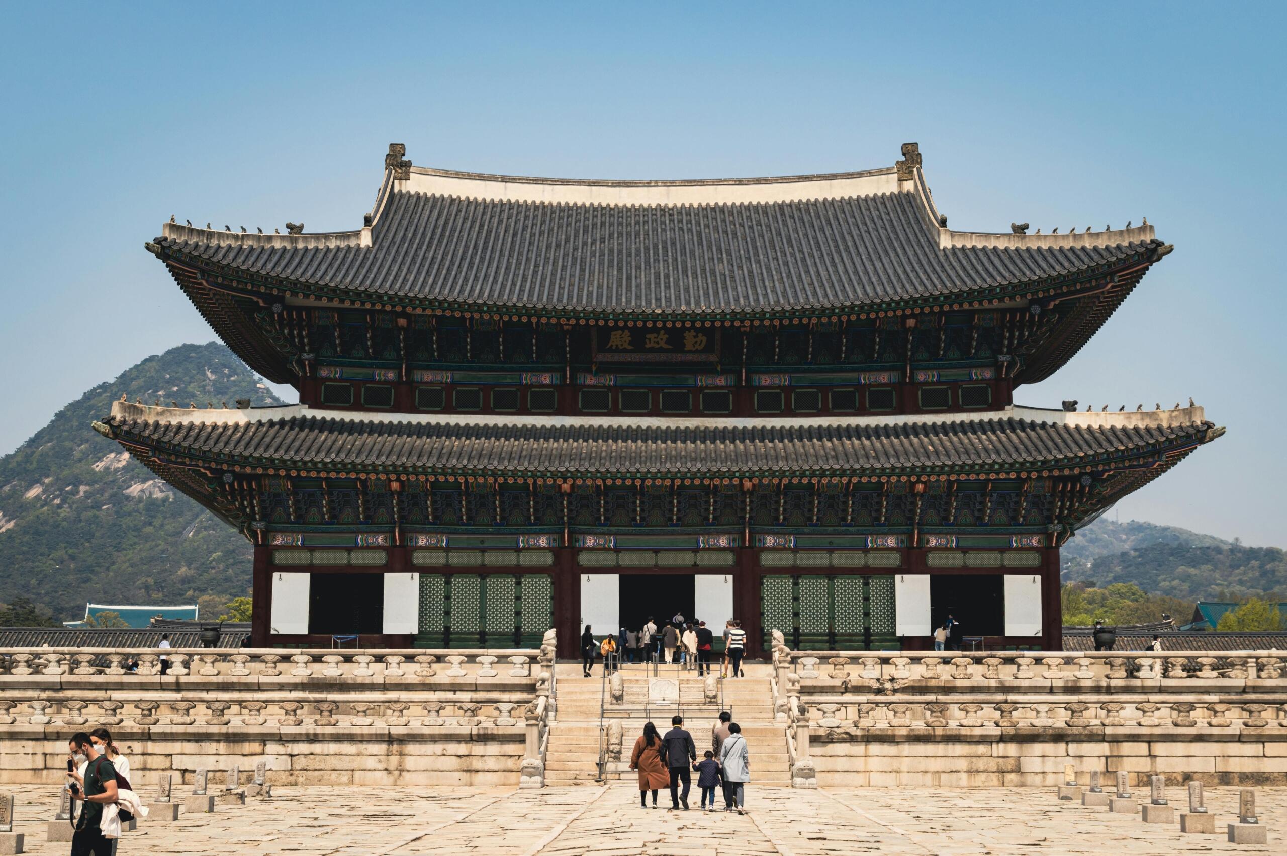 Tourists standing in front of a historic Korean palace, exploring traditional architecture and cultural landmarks during a visit to Korea.