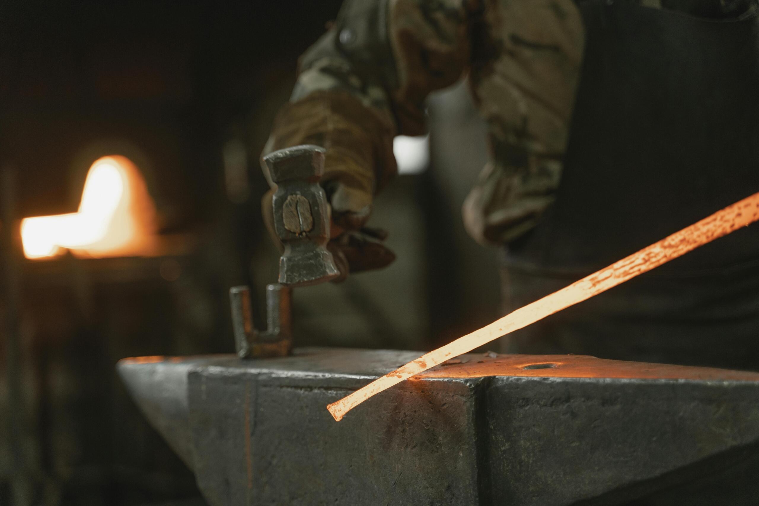 A blacksmith hammers a glowing orange metal piece on an anvil, with a forge's flames glowing softly in the background.