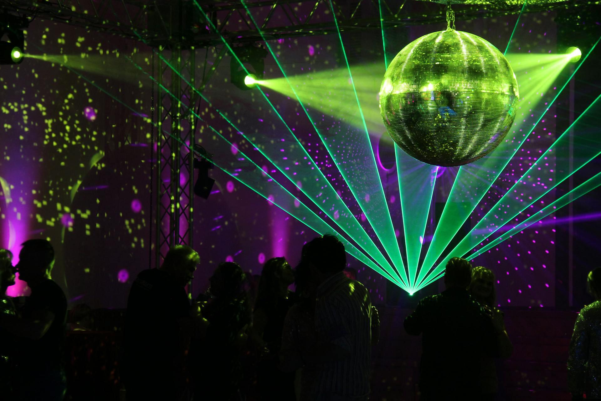 A vibrant dance floor with a disco ball reflecting colorful lights and lasers, creating an energetic party atmosphere.