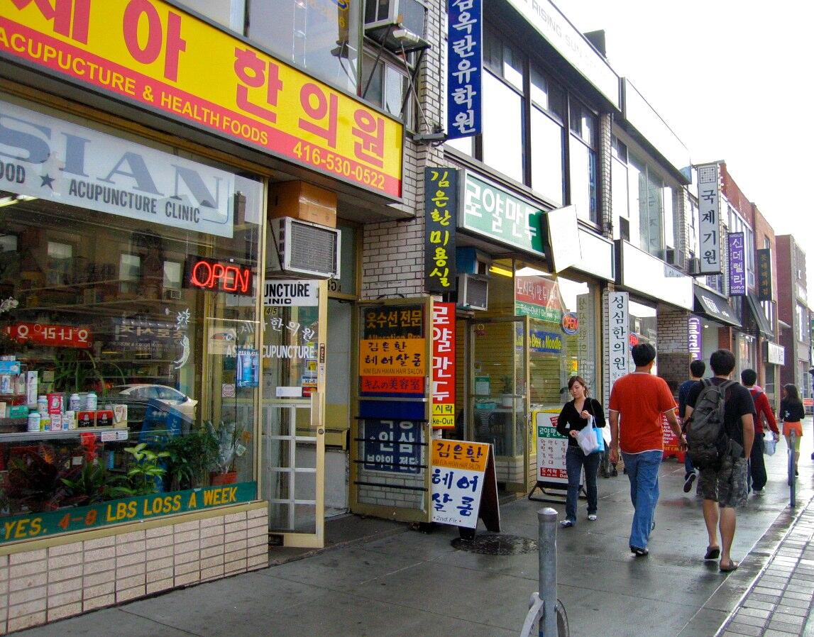 Koreatown in Toronto along Bloor Street West, showing Korean storefronts, signage, and pedestrians in a lively urban streetscape.