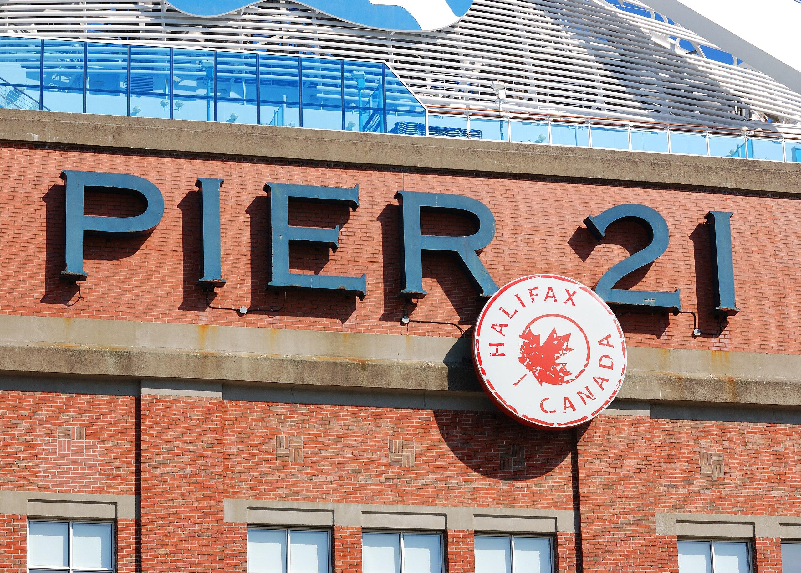 Signage of Pier 21 in Halifax, Canada, featuring large blue letters on a red brick building with a circular logo.