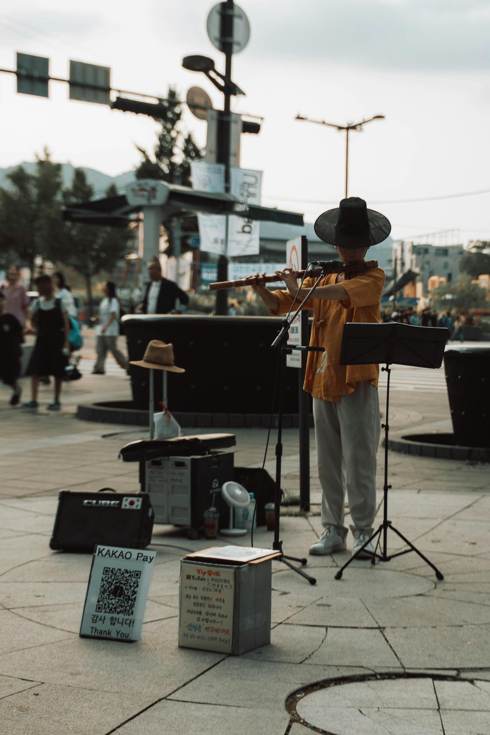 Korean street busker wearing a traditional hat, performing music during a cultural event. Source: Viridiana Rivera.
