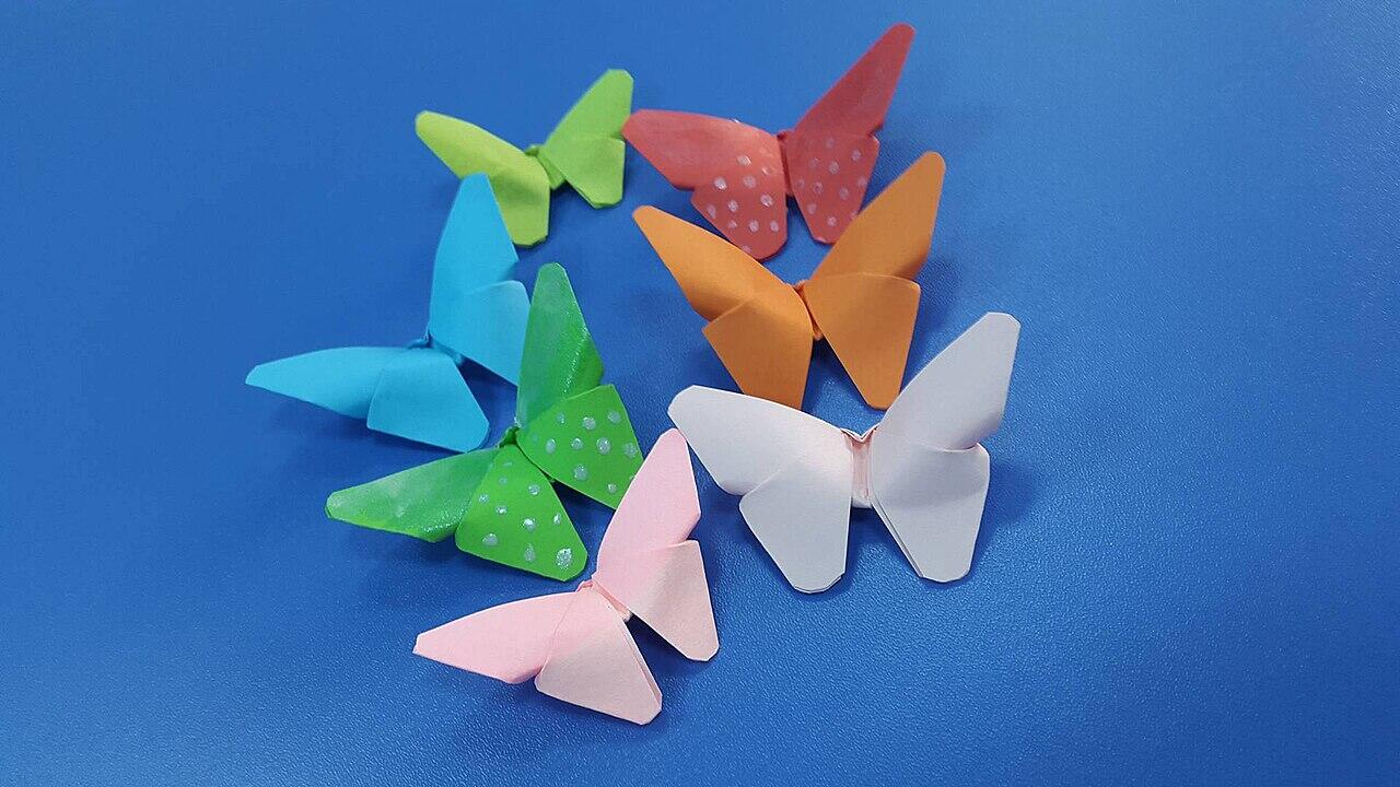 A collection of colorful origami butterflies in various shades, including blue, green, pink, orange, and white, on a blue background.