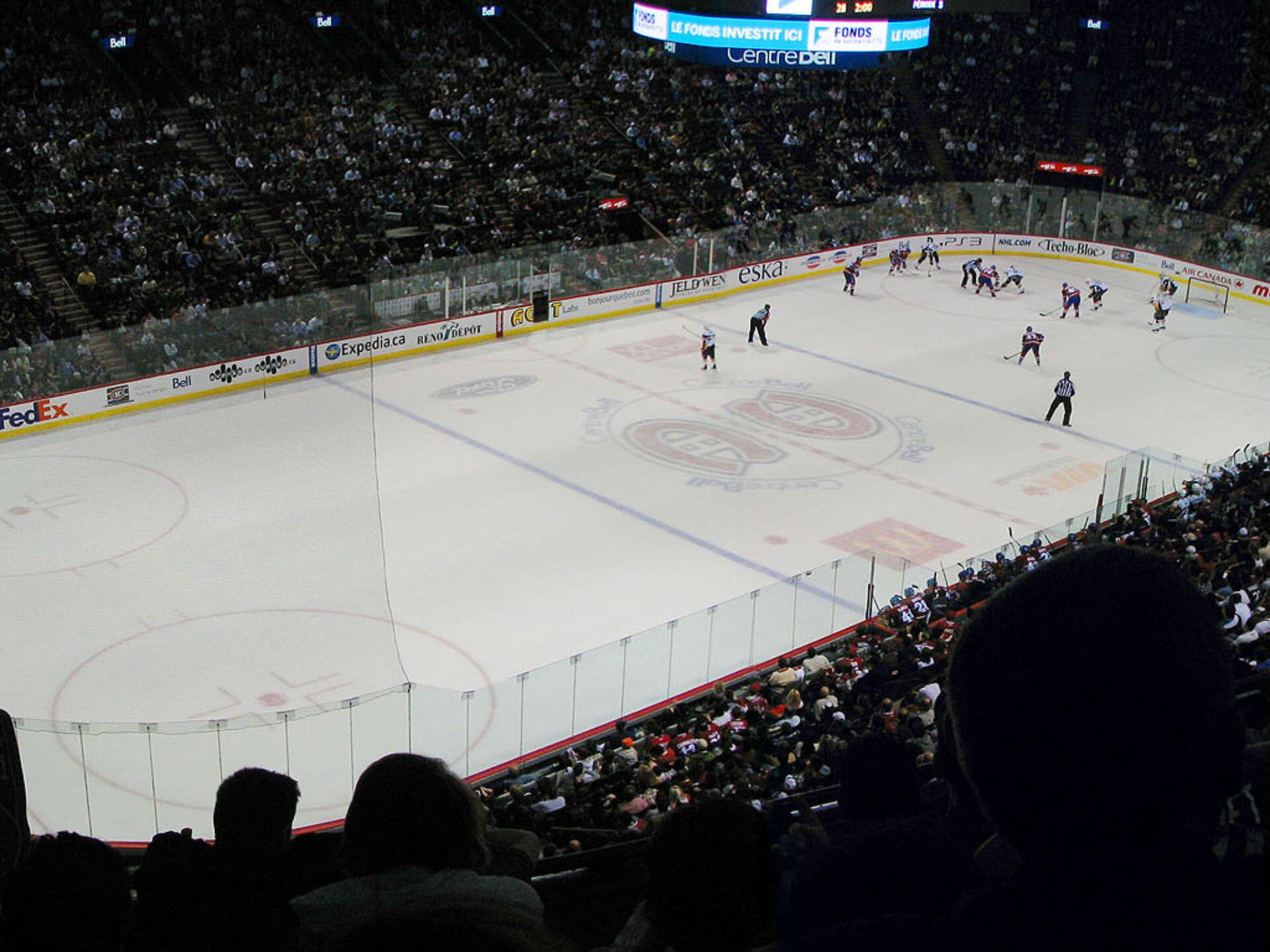 A hockey game in an indoor arena, with players on the ice and a crowded audience in the stands, captured from a high viewpoint.