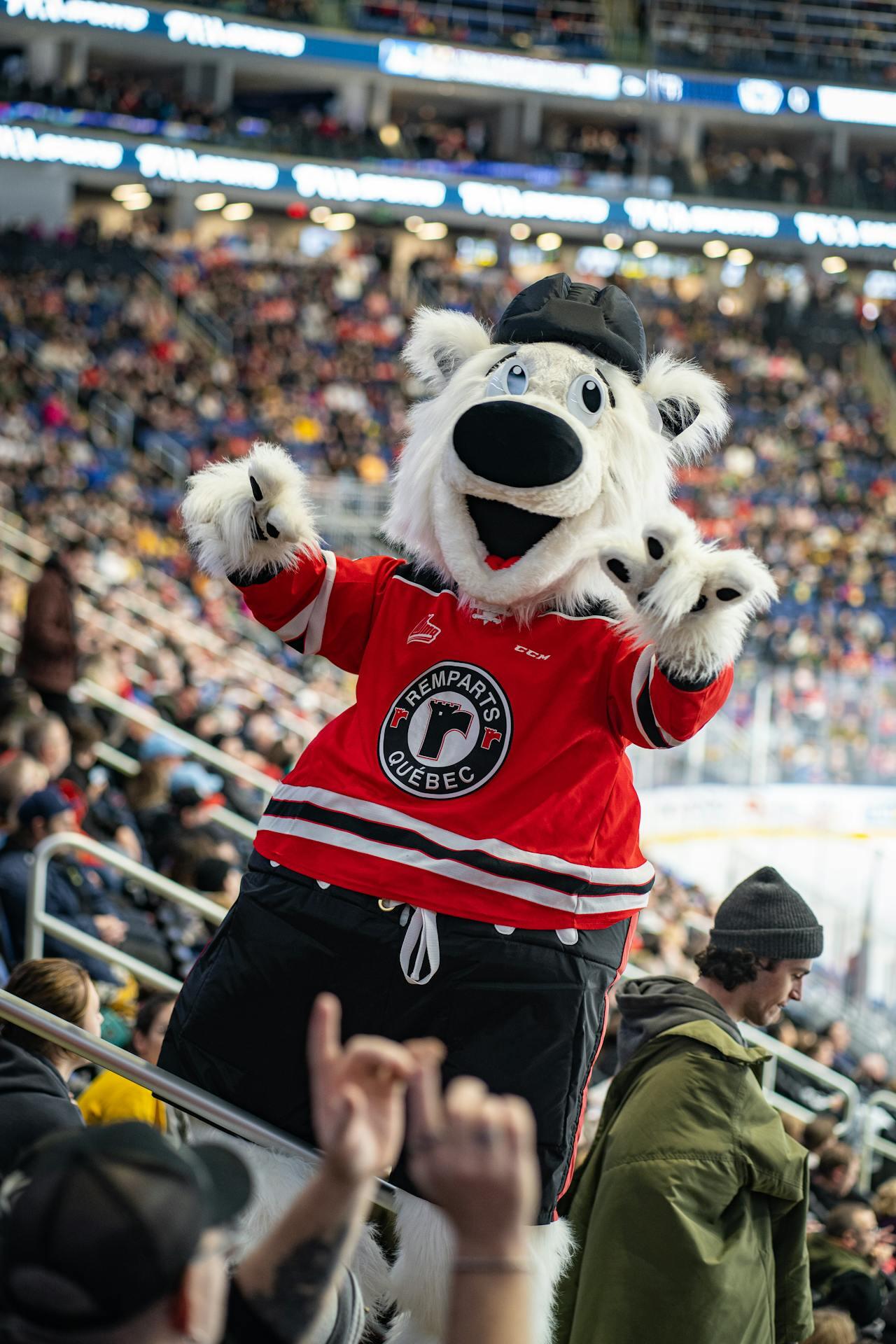 A polar bear mascot in a red hockey jersey entertains fans in a packed arena, displaying excitement and energy during a game.