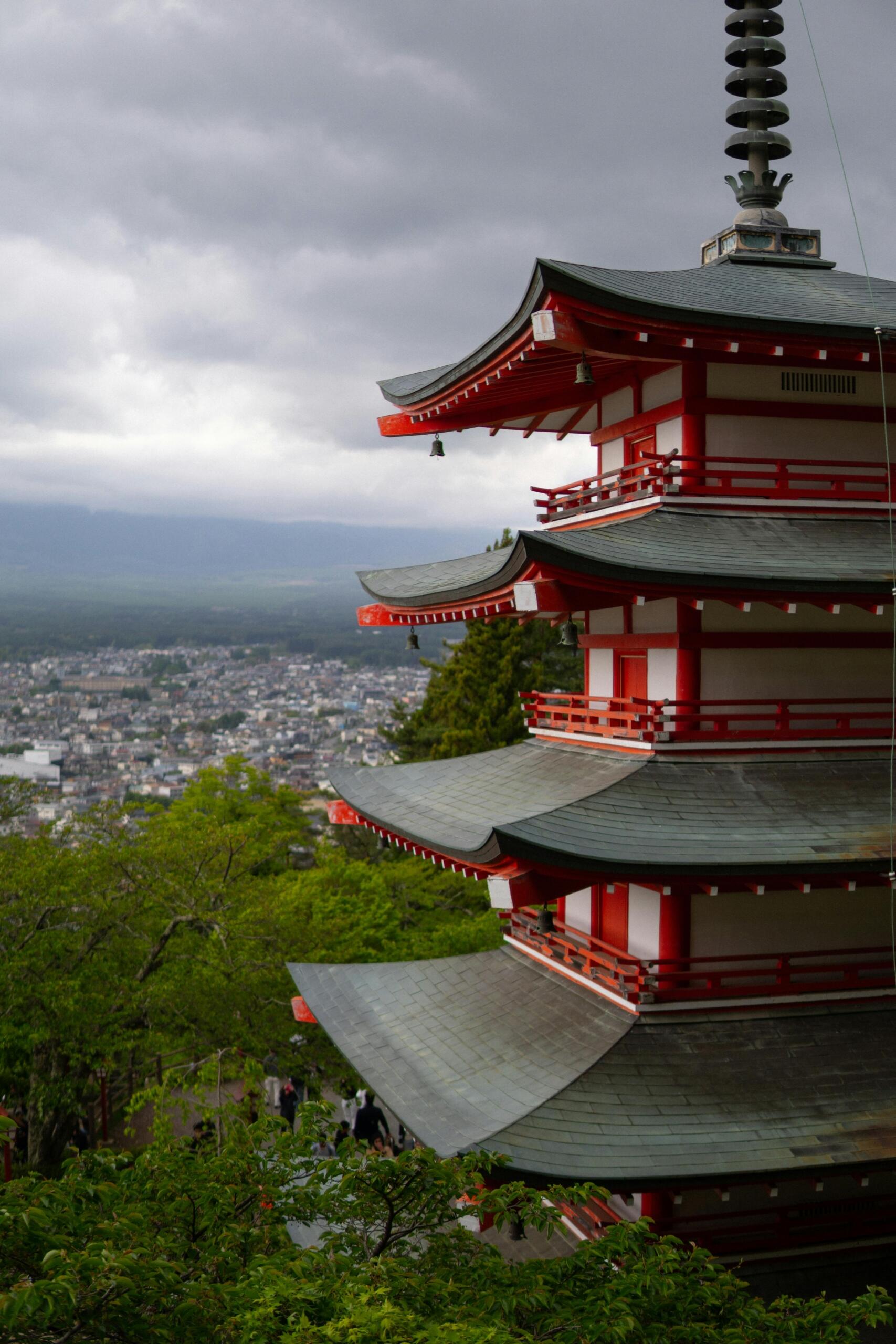 Traditional Japanese temple on a hillside overlooking a modern city, with tiled roofs and wooden architecture in the foreground and urban buildings stretching across the landscape below. Source: Talha Resitoglu.