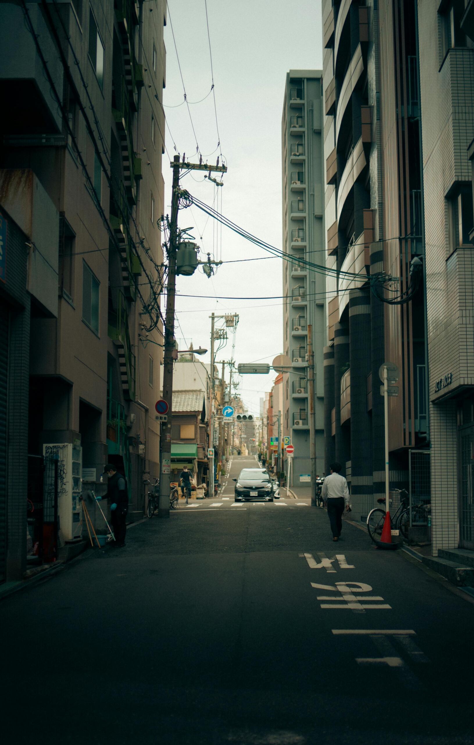 Quiet residential street in Japan lined with low-rise apartment buildings, narrow sidewalks, and parked bicycles, with no crowds and a calm neighborhood atmosphere. Source: Tama Utama.