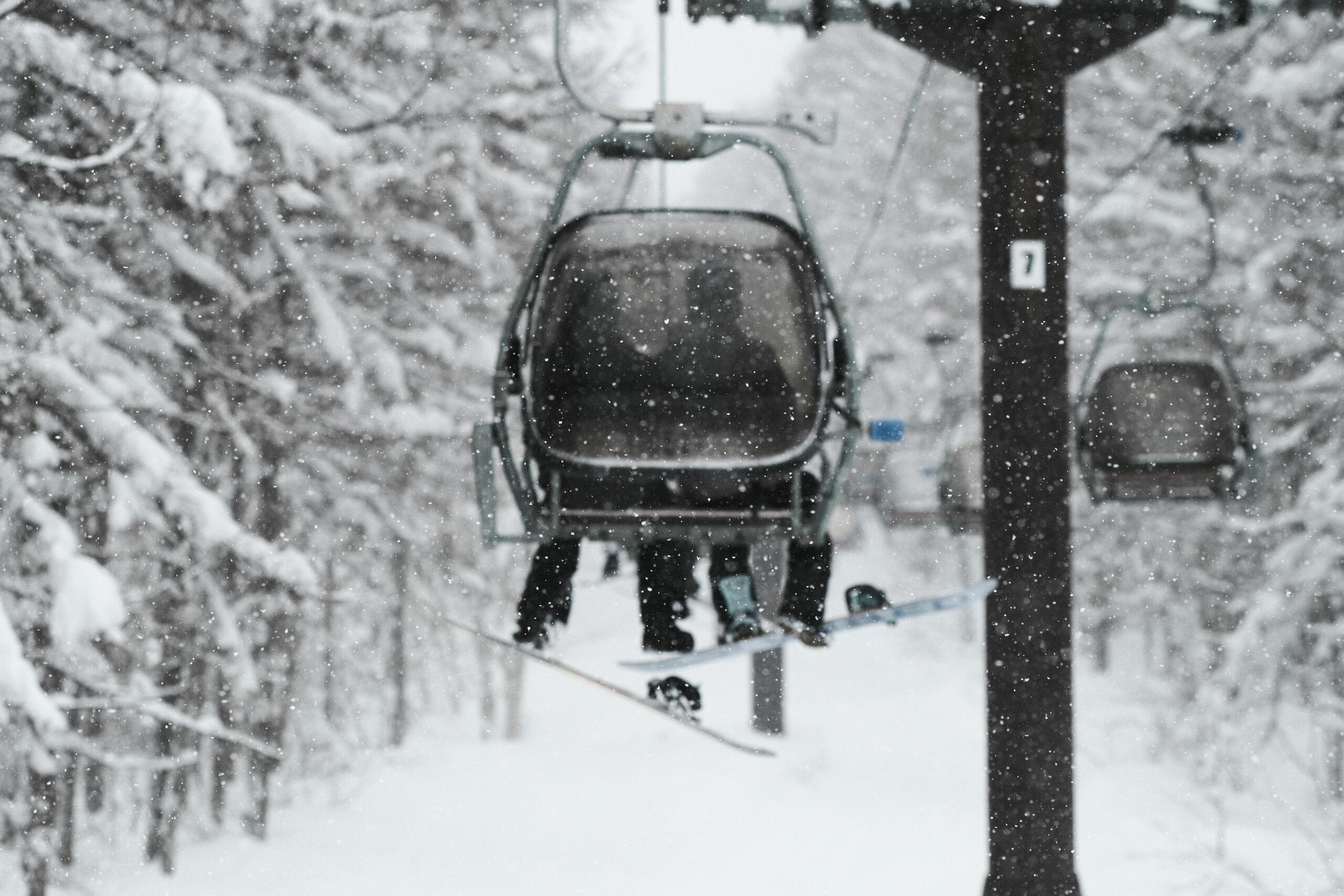Ski lift carrying people up a snowy mountain on a winter day, with snow-covered trees and a cloudy sky in the background.