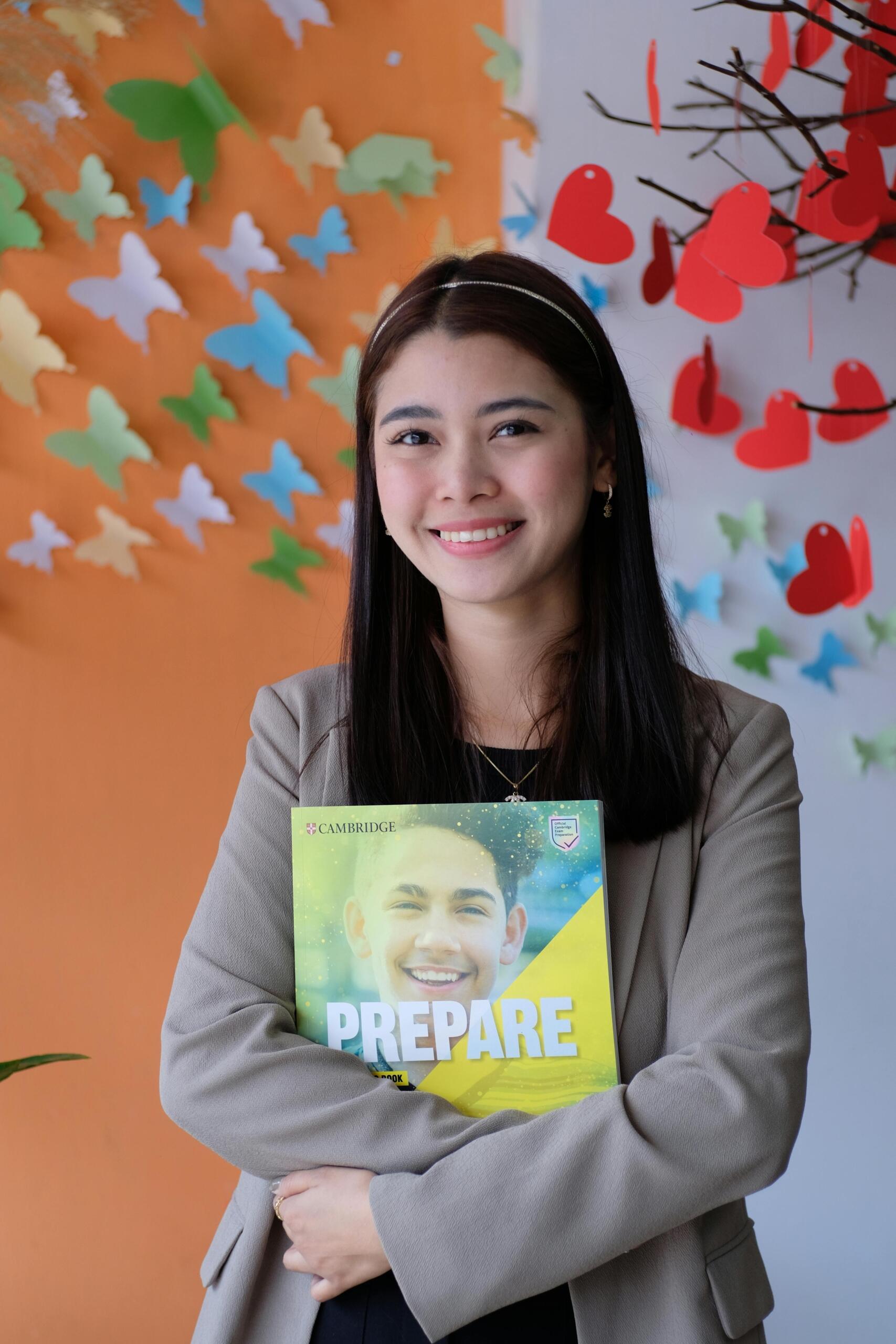 Girl standing and holding an English textbook, looking ready to study in a classroom or learning environment. Source: Ngo Chuy.