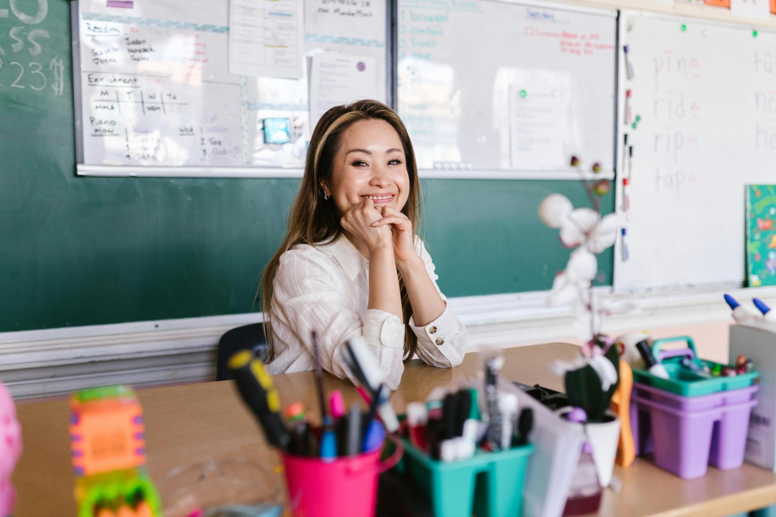 Teacher sitting at a desk in a classroom, reviewing papers and preparing lesson materials in a quiet educational setting.
