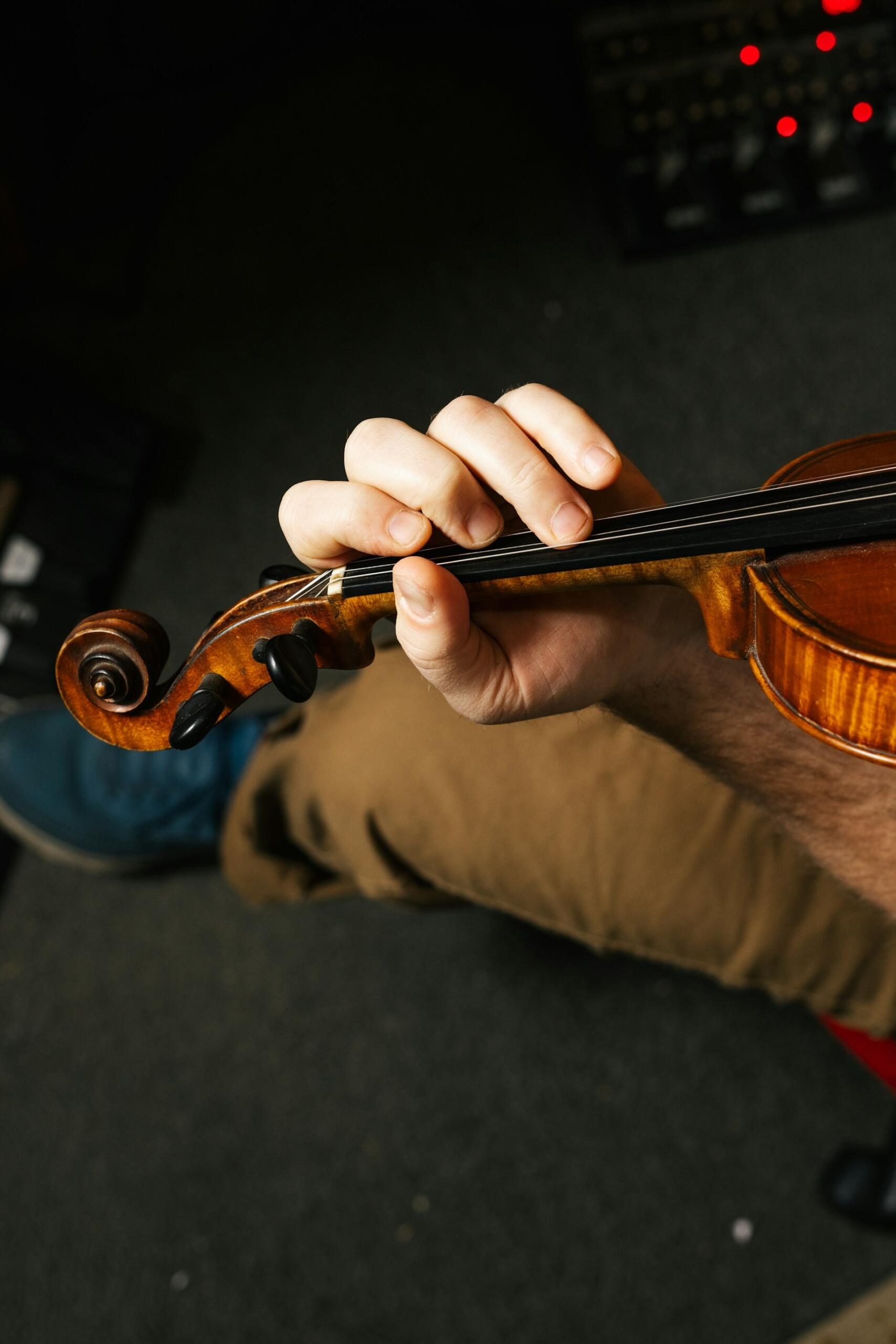 Close-up of a musician’s hand fingering the strings of a polished violin.