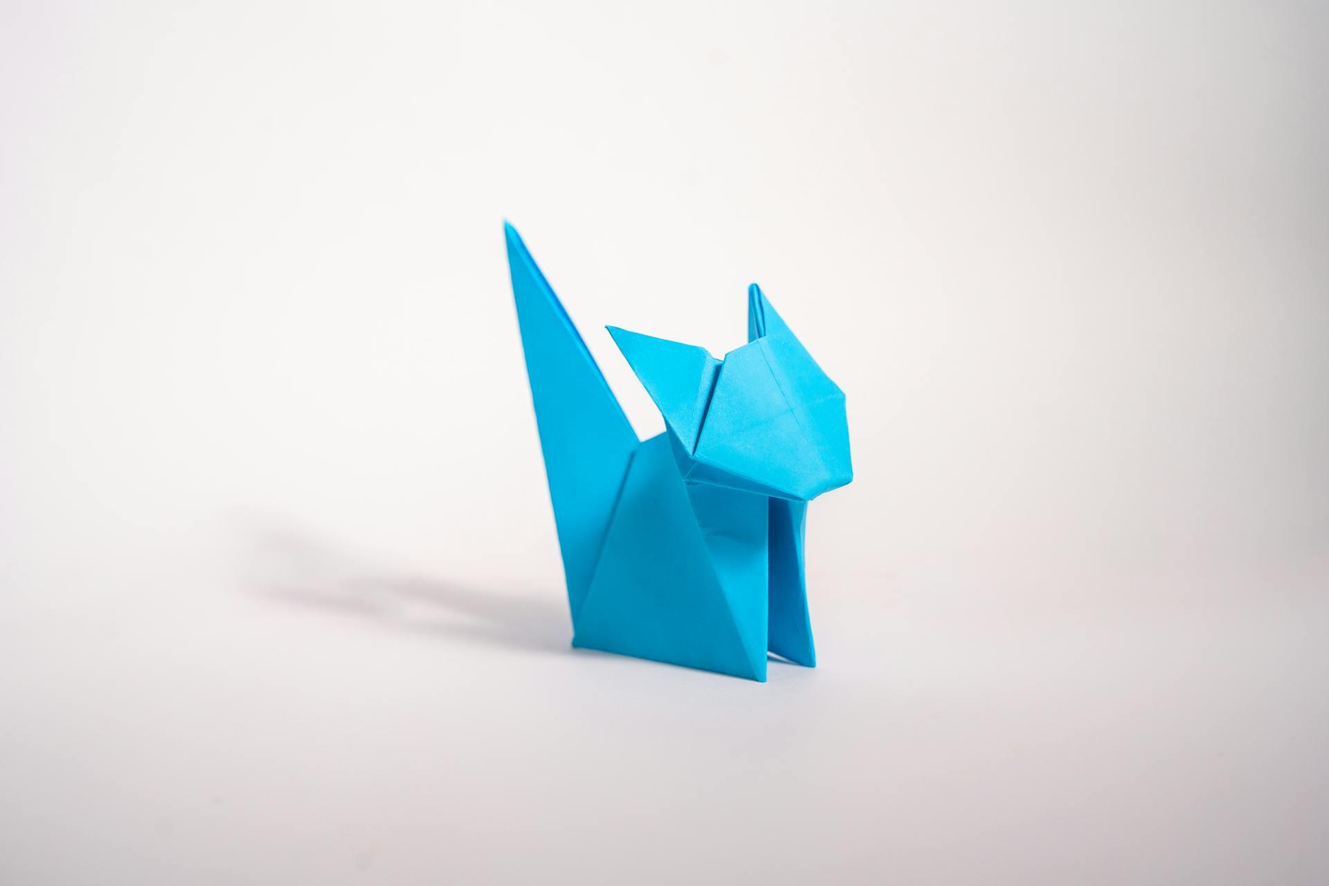 A vibrant blue origami cat sculpture stands against a plain, light background, showcasing intricate folding and geometric shapes.
