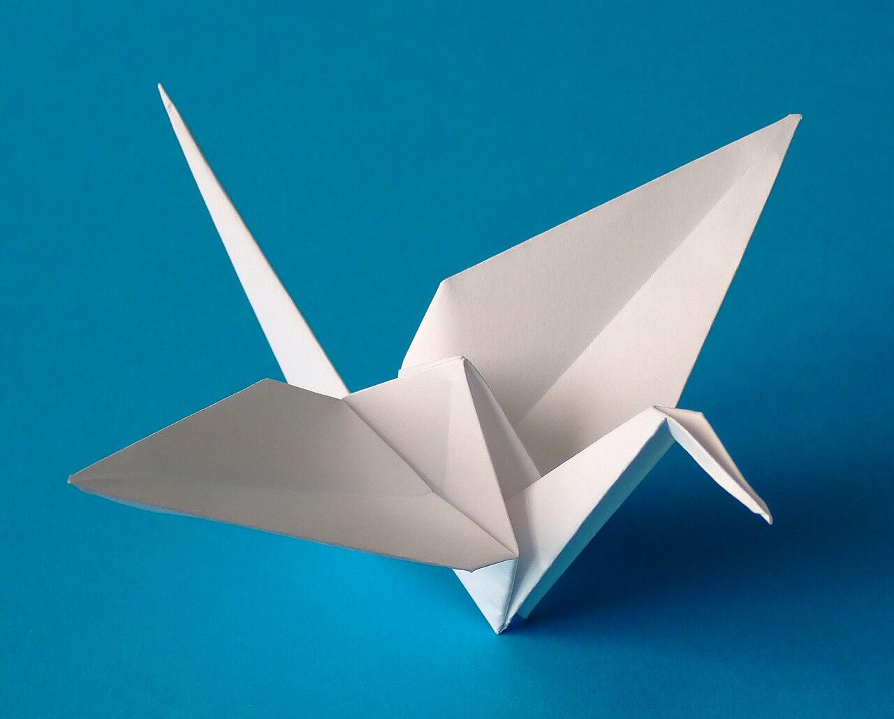 A delicate white origami crane with outstretched wings, set against a vibrant blue background.