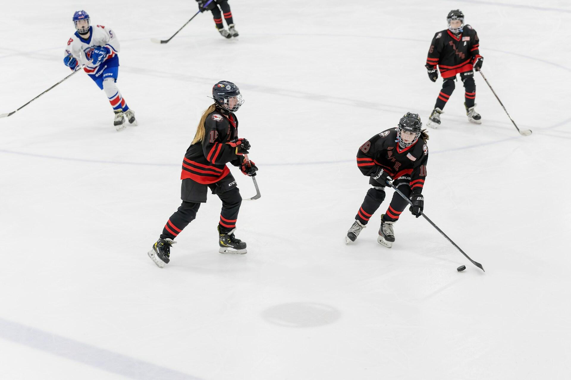 Youth ice hockey scene featuring players in black and red jerseys, in an action-packed game on the rink.