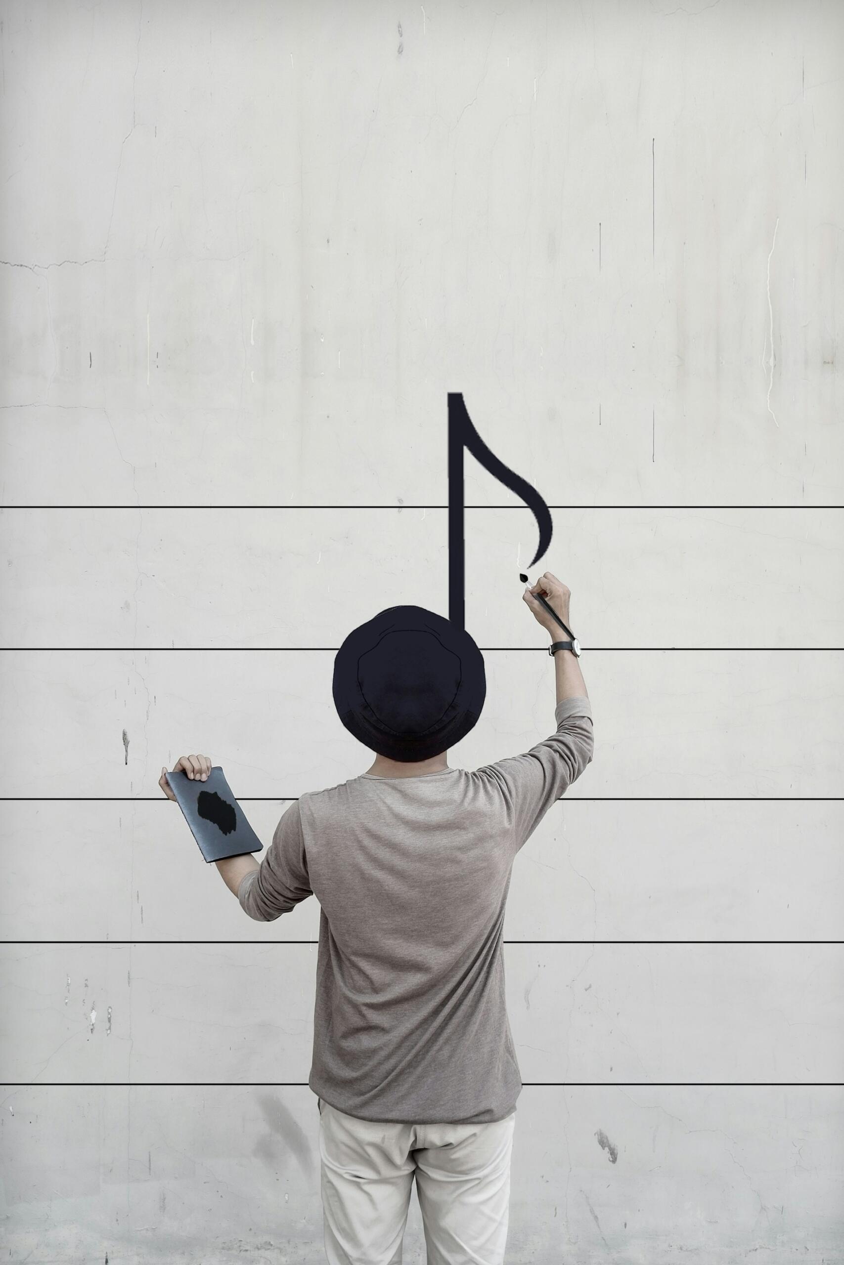 Person in a hat paints a large black musical note on a lined, weathered wall while holding a paintbrush and palette.