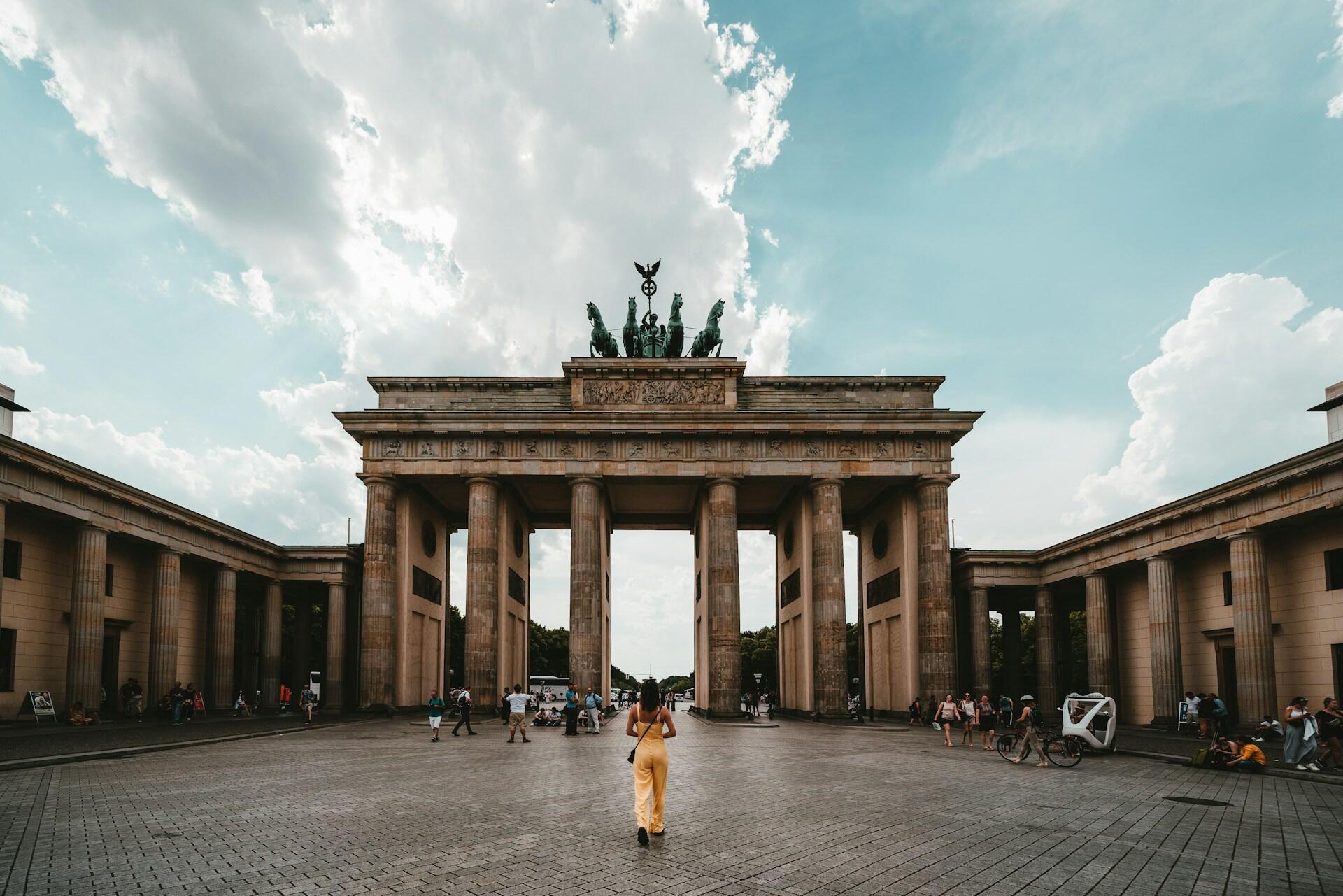 Brandenburg Gate in Berlin with people walking around under a cloudy blue sky.