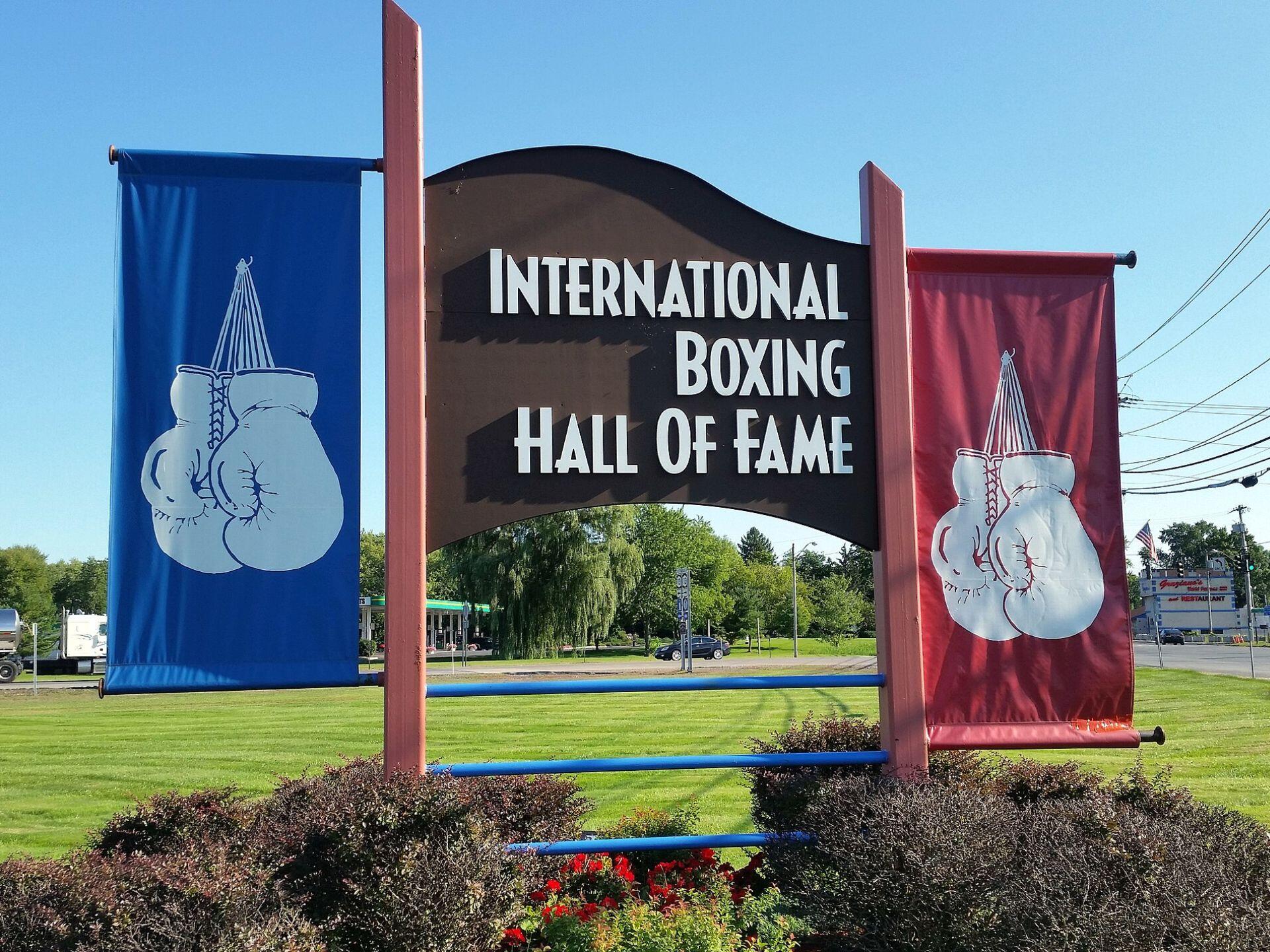 Sign for the International Boxing Hall of Fame with banners featuring white boxing gloves on blue and red backgrounds.