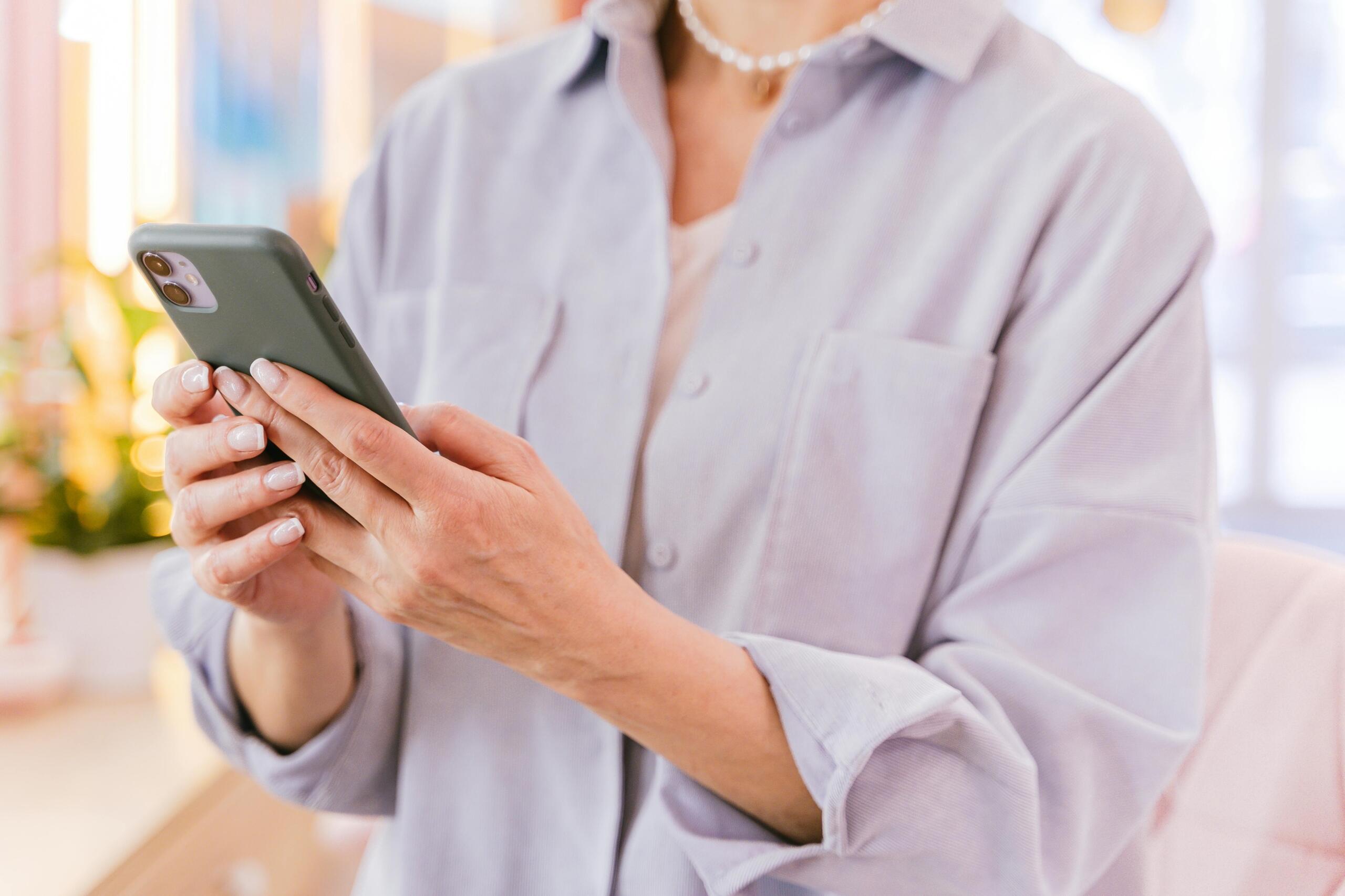 Woman looking at a smartphone screen while standing indoors, focused on reading or using a mobile app.