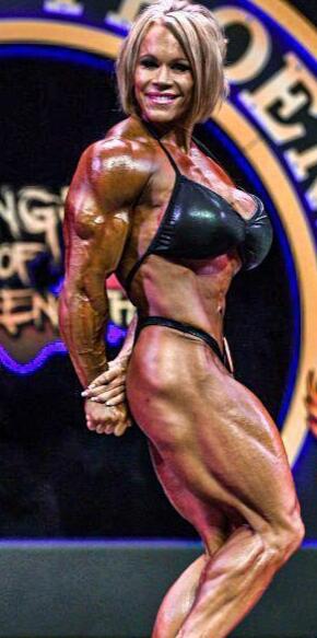 A muscular figure in a black bikini poses on stage, showcasing defined arms and legs, with a competition backdrop.