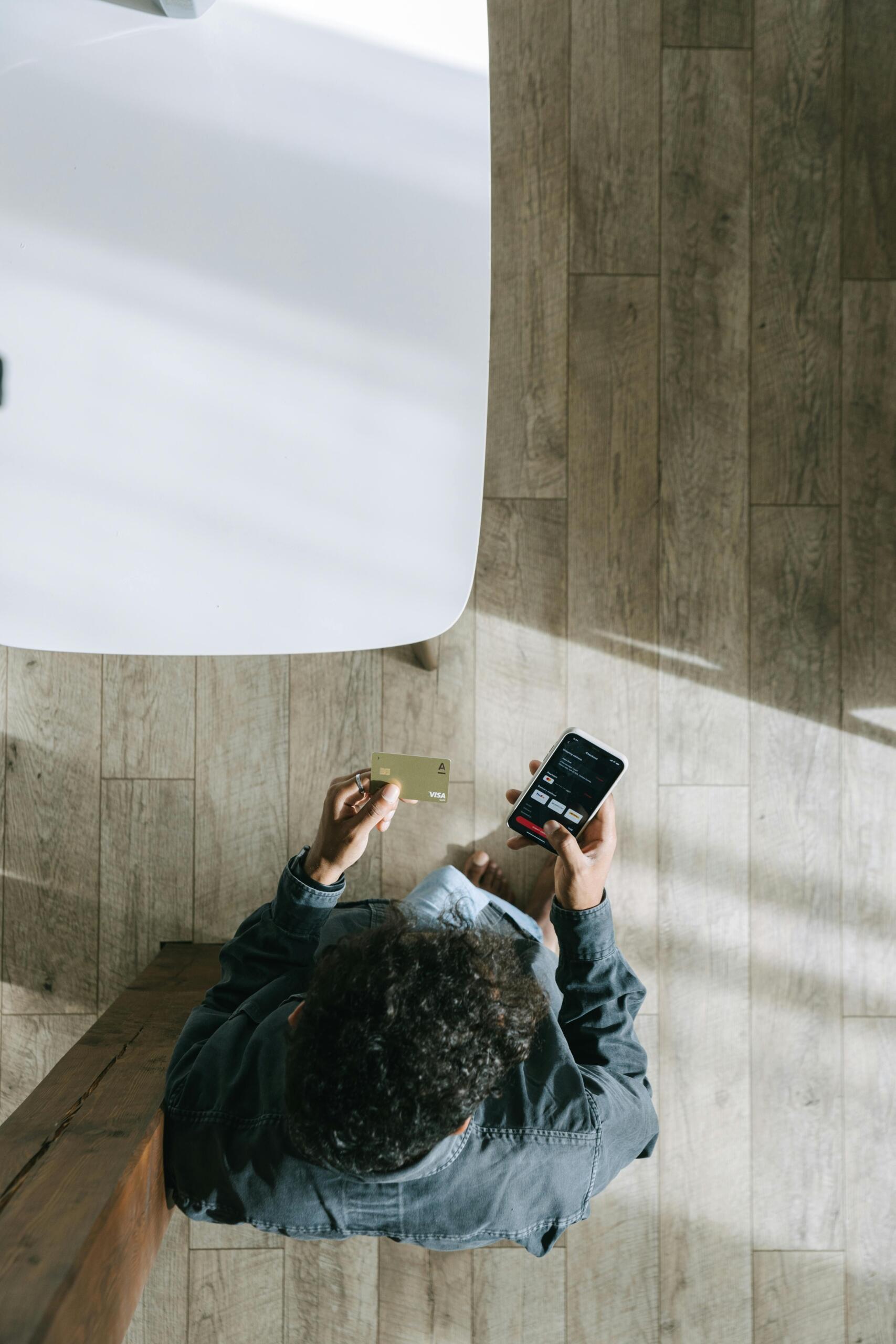 Man holding a credit card while using a smartphone to make a payment, viewing a finance app during a transaction.