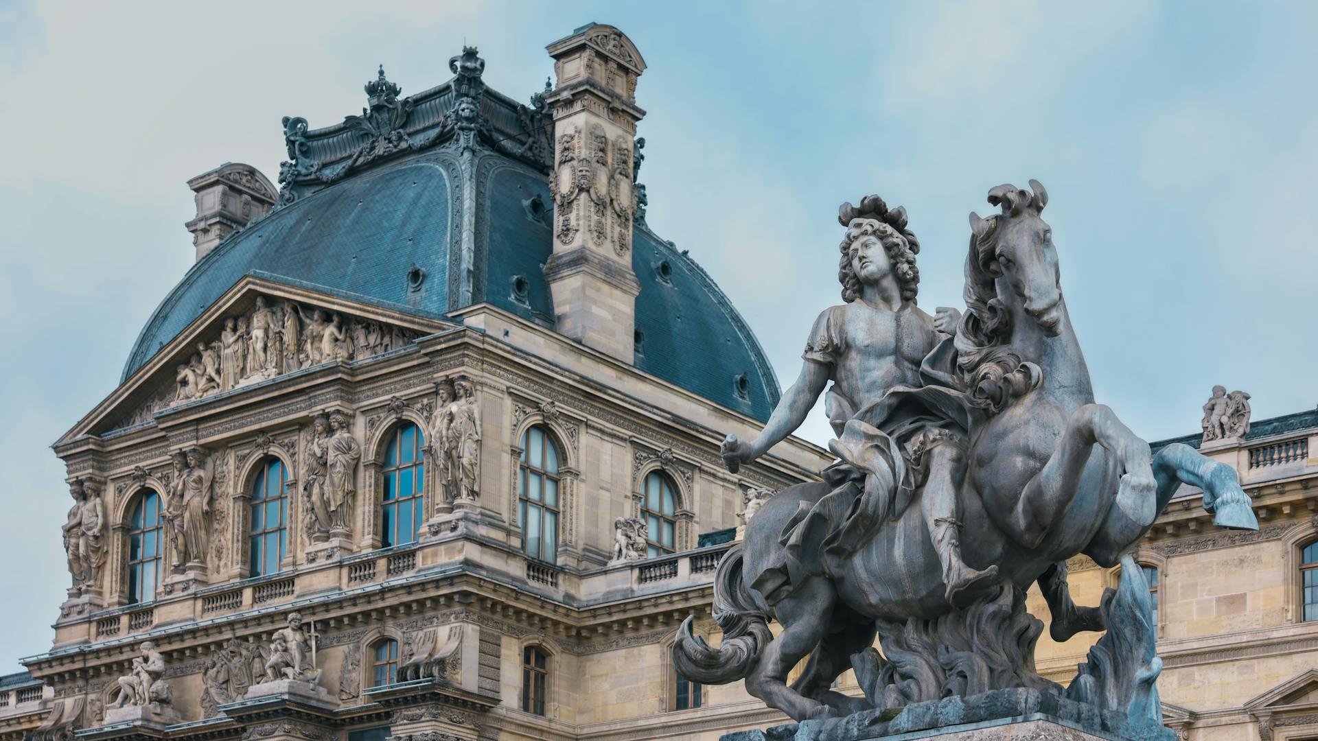 Bronze equestrian statue of a figure with curly hair in front of an ornate, classical building with sculpted reliefs and arched windows.