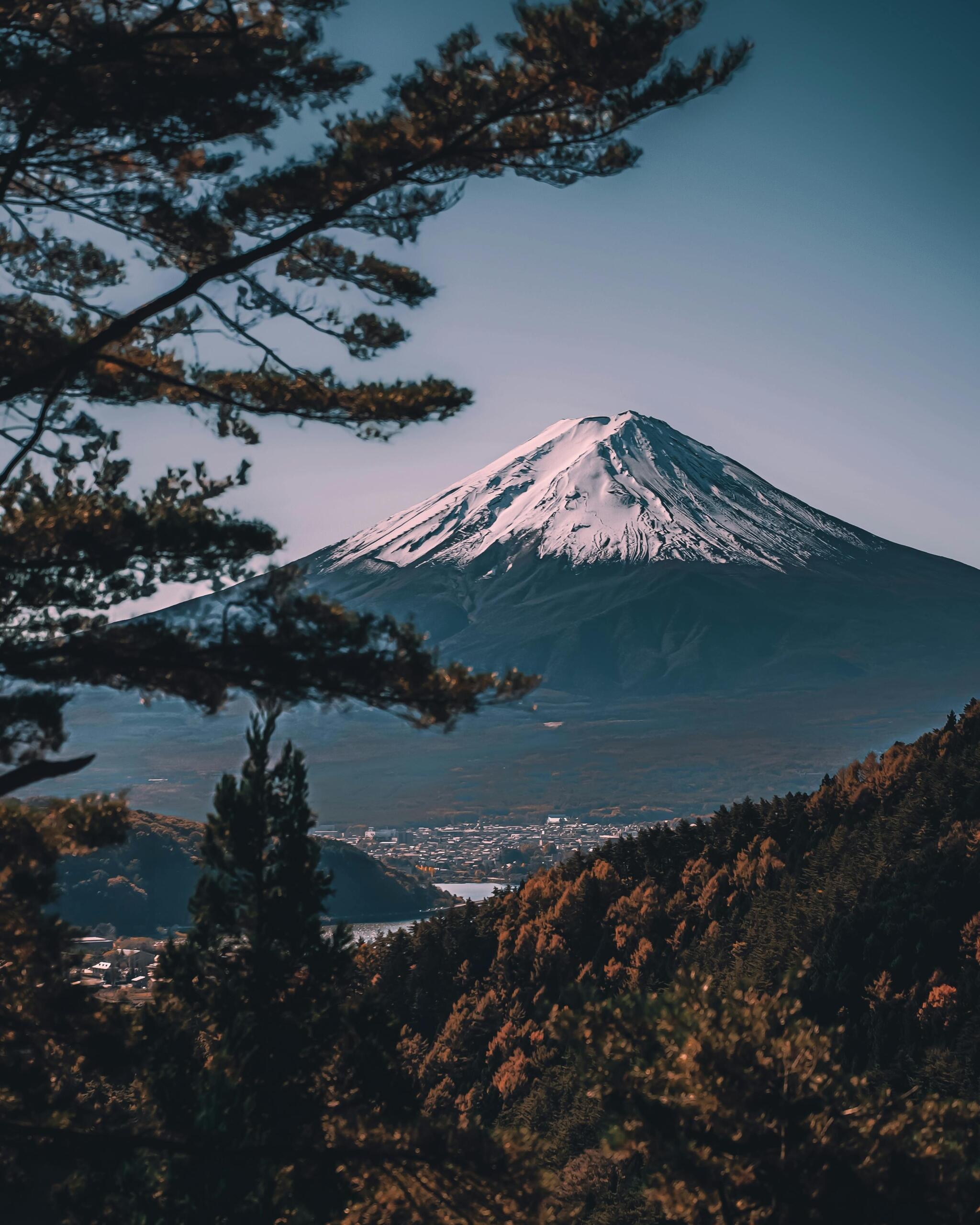 Scenic photo of Mount Fuji with its snow-capped peak rising above the surrounding landscape under a clear blue sky. Source: K. K.