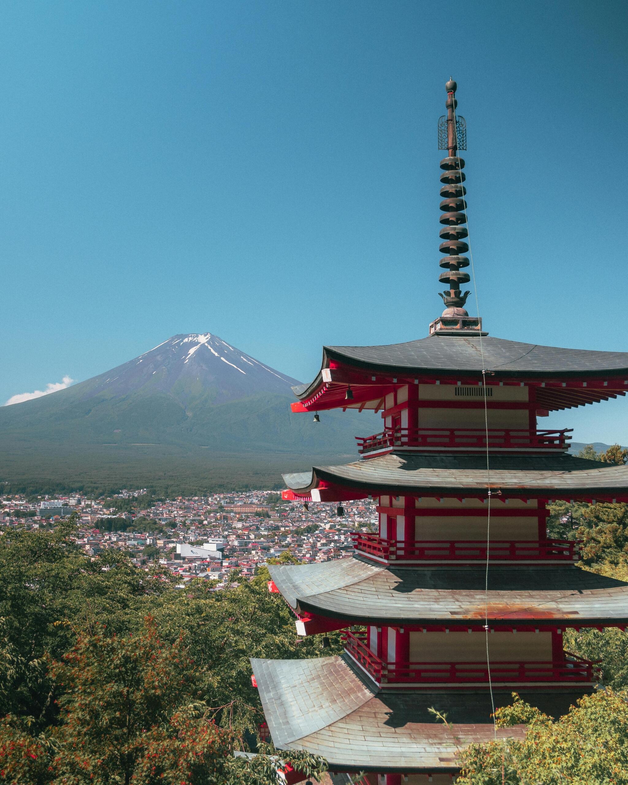 Traditional Japanese temple in the foreground with a mountain rising behind it, surrounded by trees and natural scenery under a clear sky.