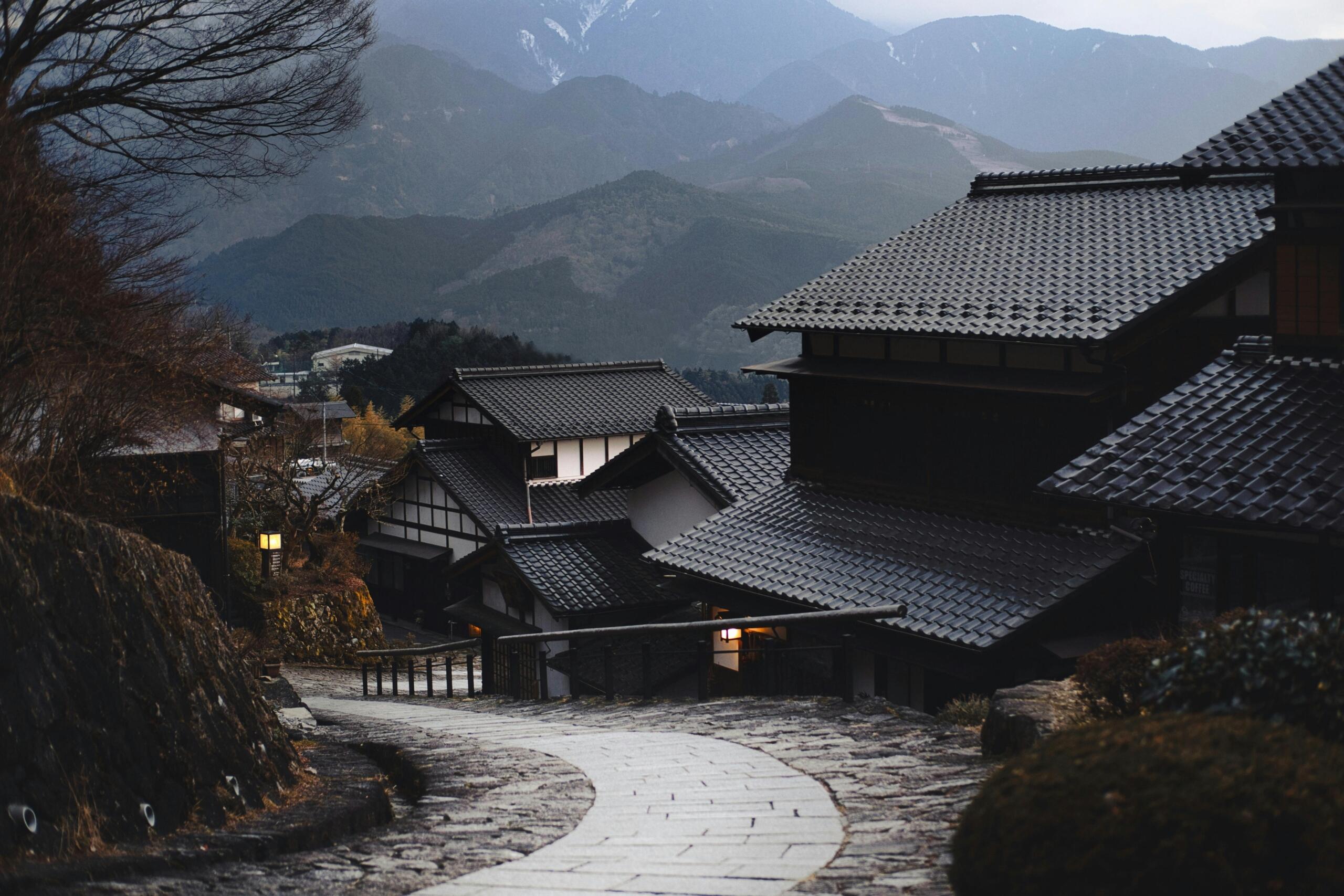 Historic street in Japan lined with traditional wooden buildings, narrow stone pathways, and hanging lanterns, creating a preserved old-town atmosphere.