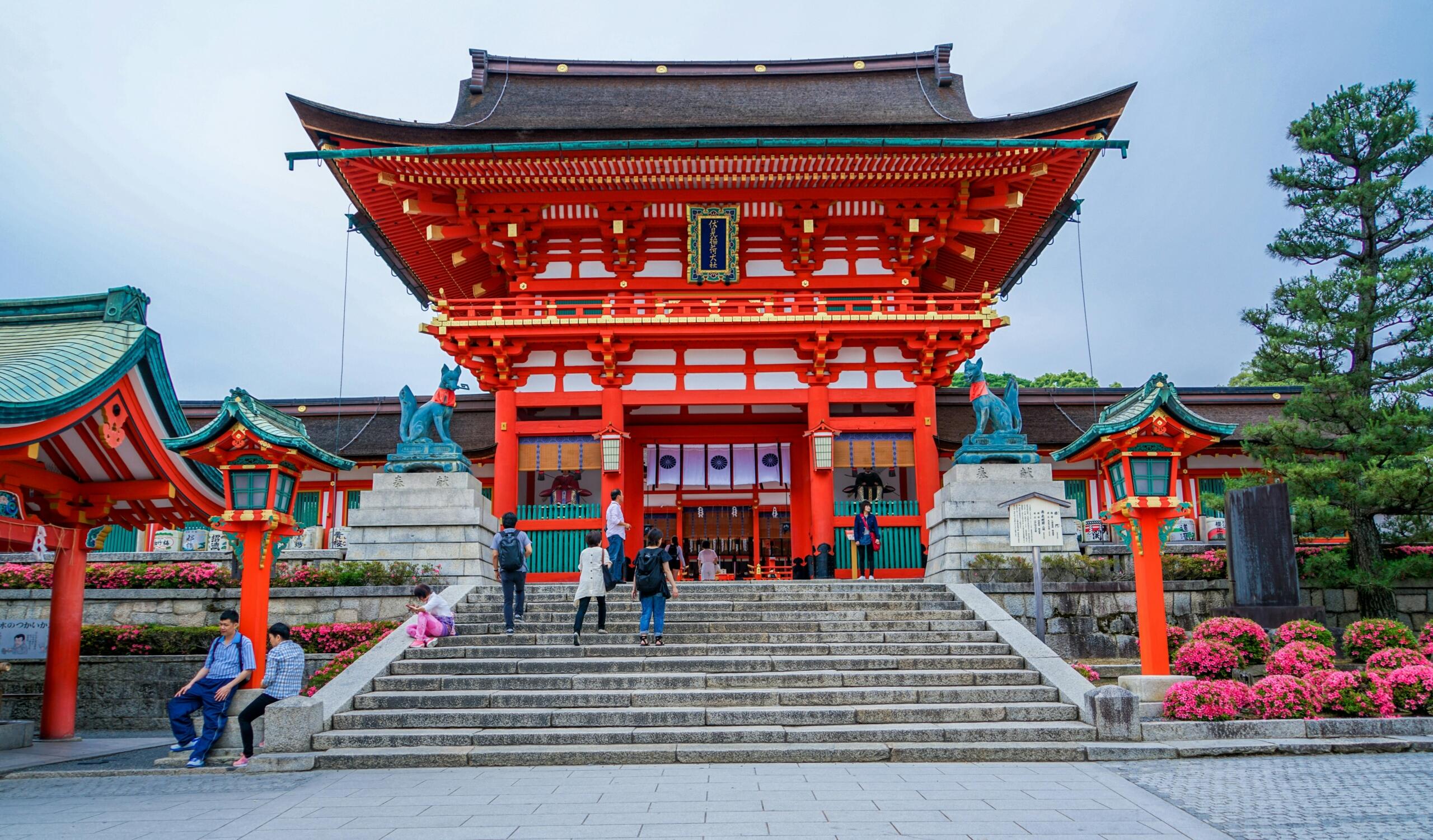 Bright red Japanese temple with traditional curved roofs and decorative details, set against a clear sky and surrounded by peaceful grounds.
