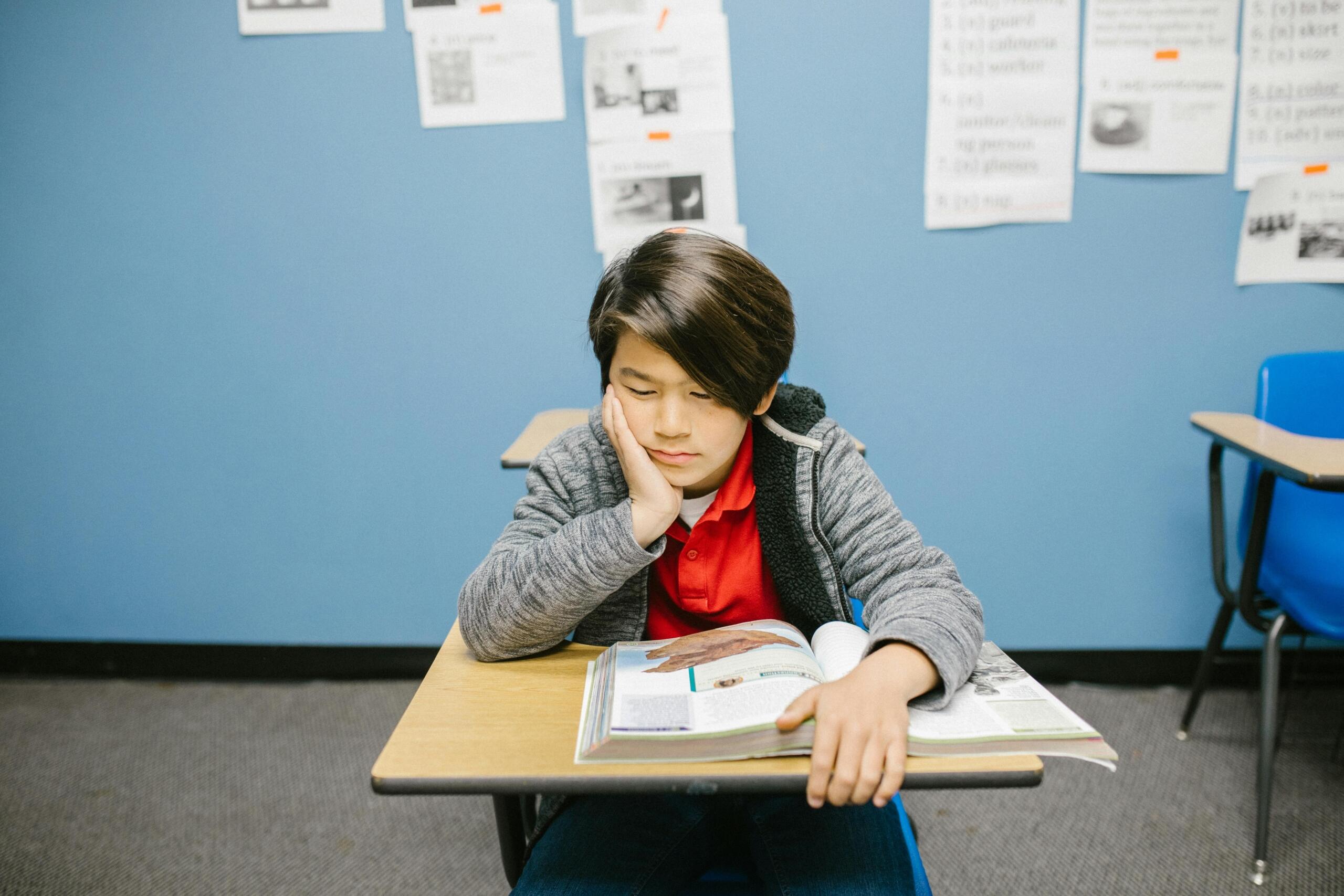 Japanese boy sitting at a classroom desk, focused on his work with notebooks and school materials in front of him.