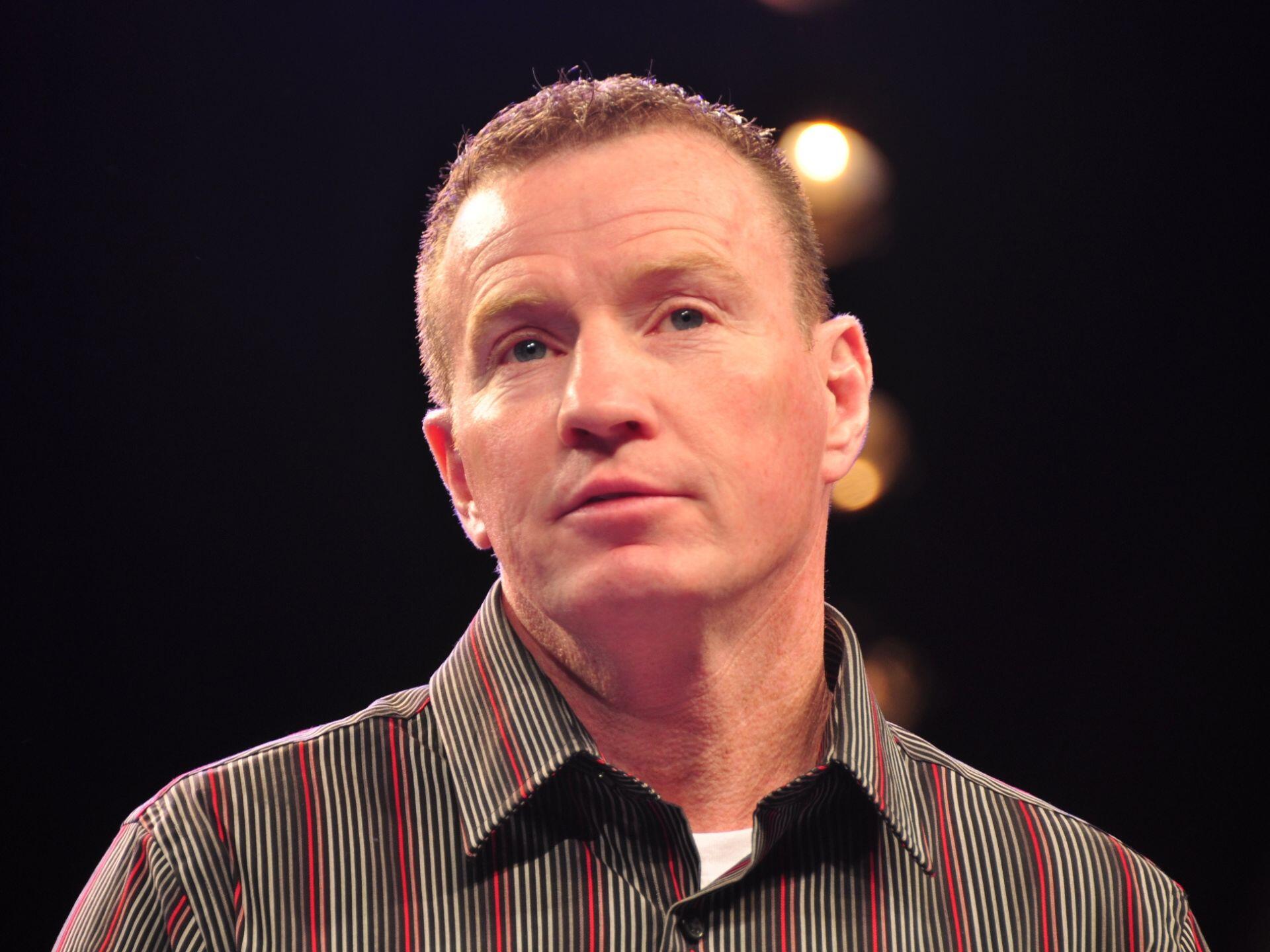Man wearing a striped button-up shirt against a dark background with blurred lights.