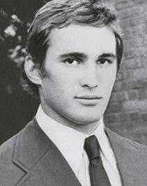 A black and white photo of a man in a suit and tie, standing outdoors with a blurred face.