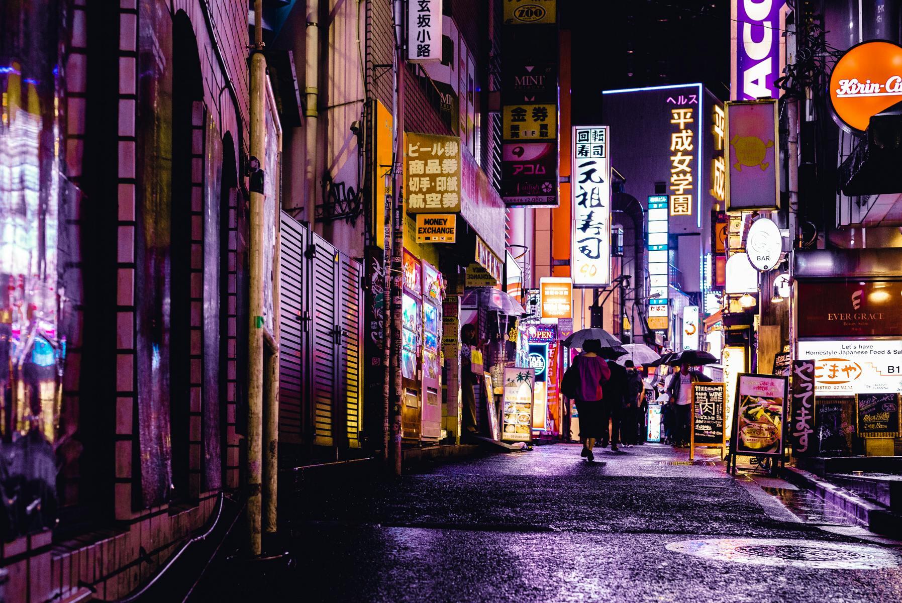 Cityscape in Japan at night with illuminated buildings, glowing neon signs, and streets lit by lanterns and streetlights.