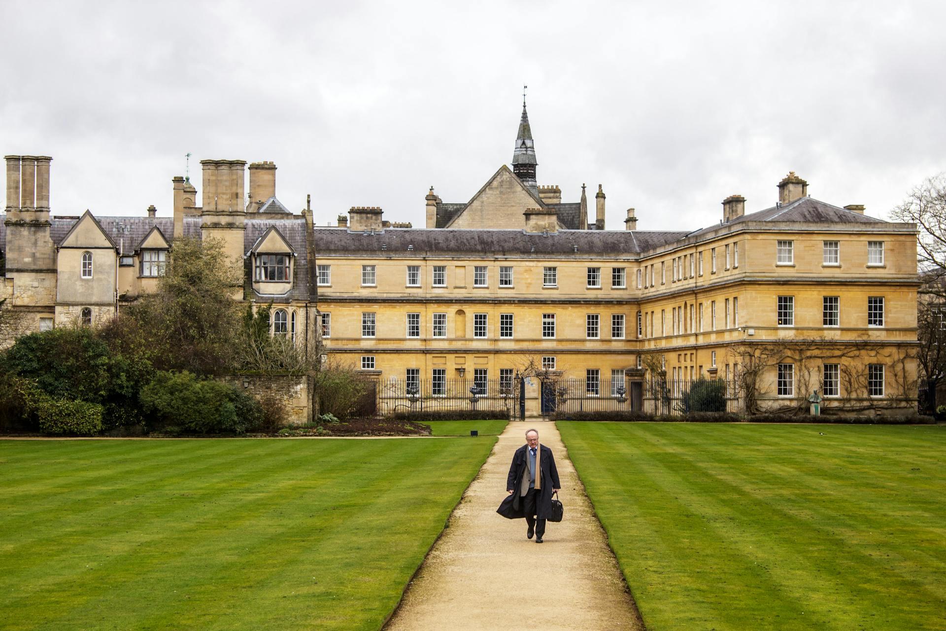A person walks along a path in front of a large, imposing building under a clear blue sky.