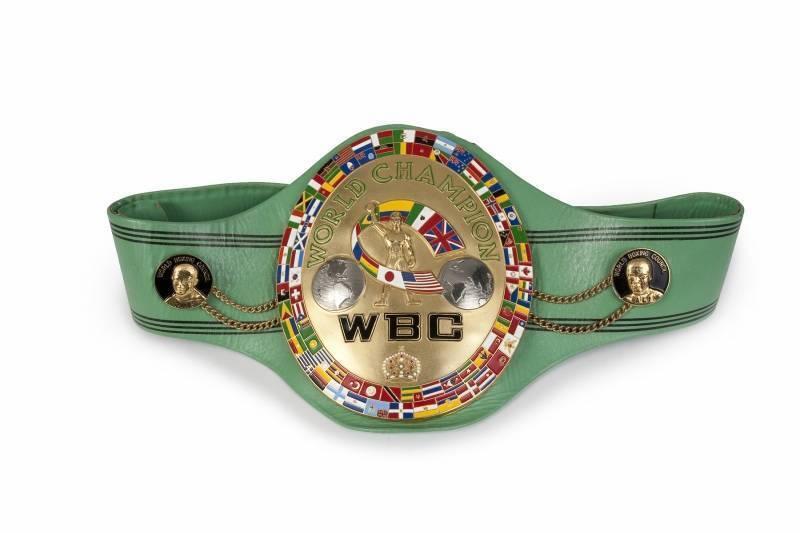 A green championship belt with a gold center displaying "WORLD CHAMPION" and "WBC," surrounded by flags from various countries.