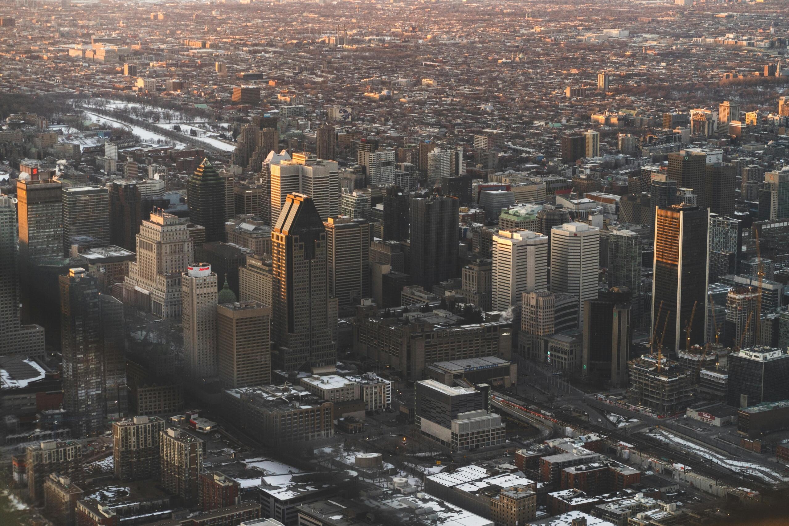 Panoramic view of Montreal at dusk with glowing city lights, high-rise buildings, and a colourful evening sky fading behind the skyline.