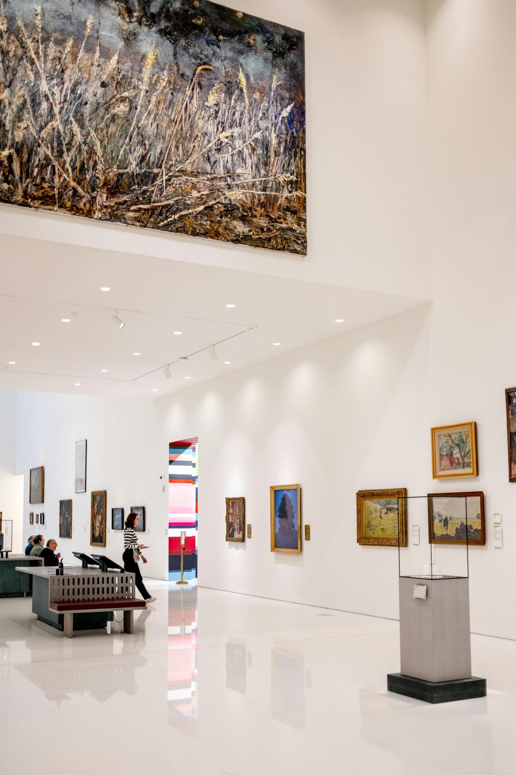 Bright museum gallery with white walls displaying framed paintings, polished floors, and a quiet open space for visitors to view the artwork. Source: Pexels.