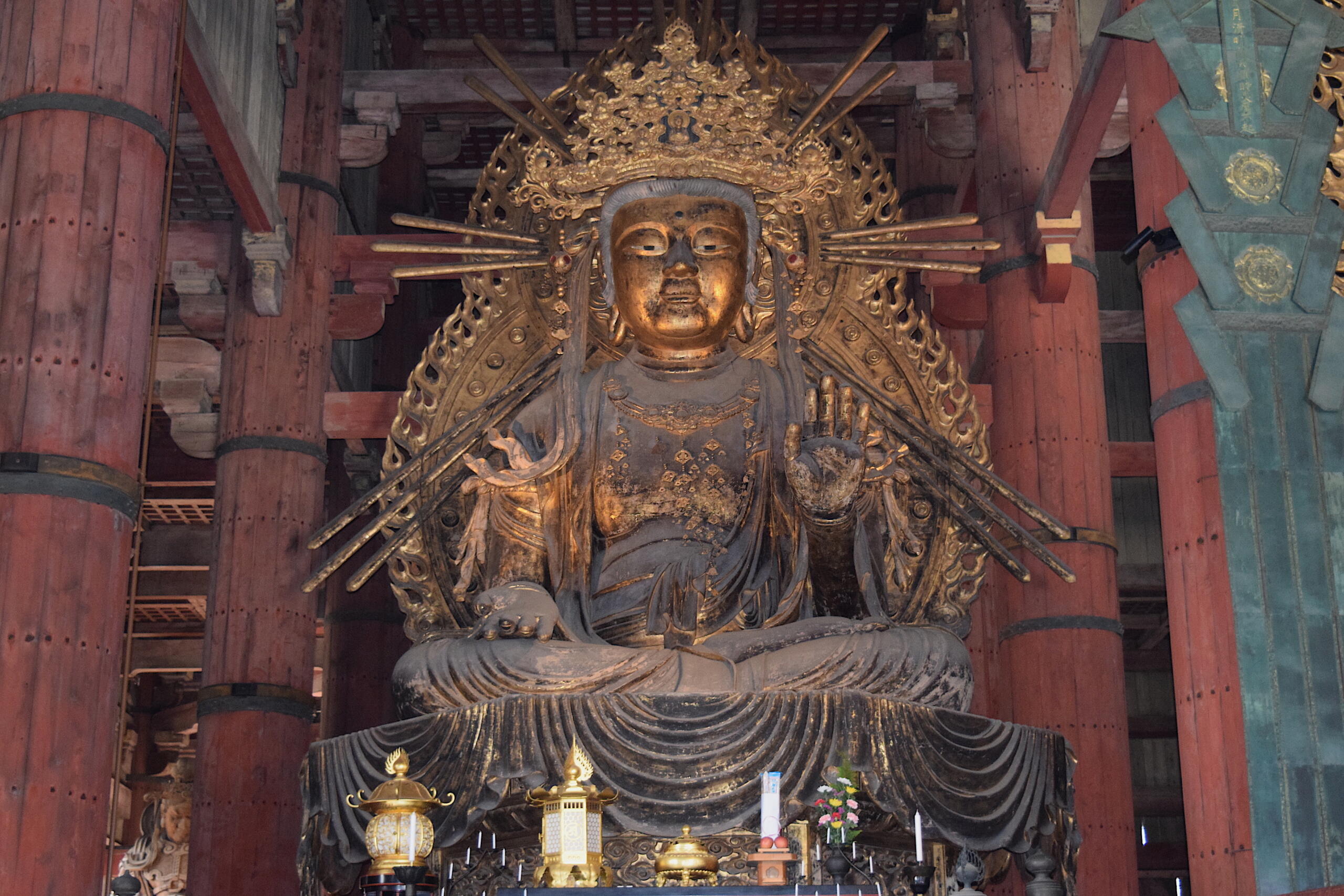 Alt text: Large golden Buddha statue seated in lotus pose inside a temple with ornate backdrop and red pillars.