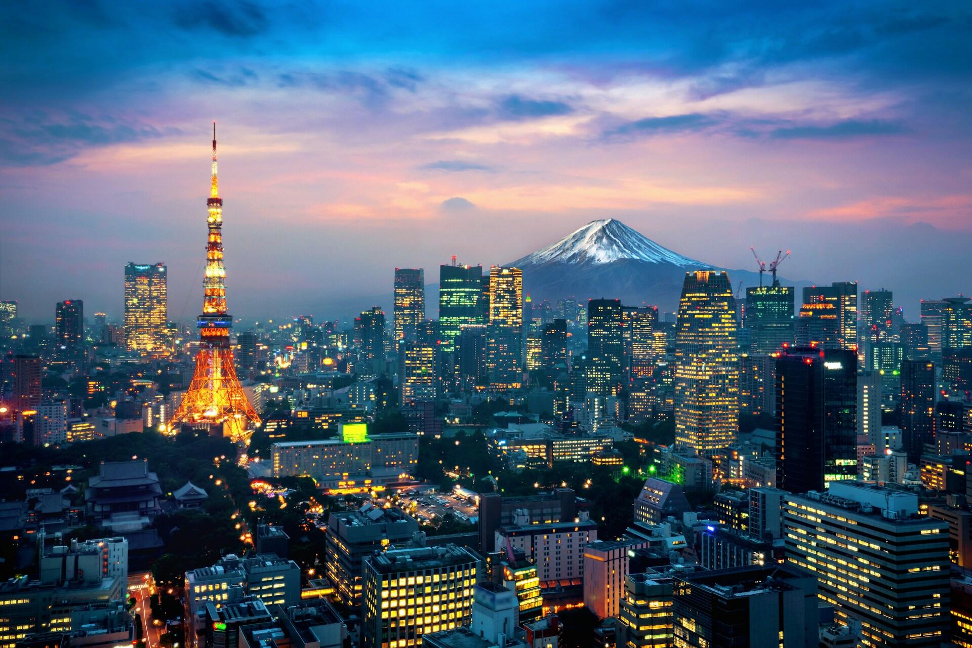 Tokyo cityscape at dusk with illuminated Tokyo Tower and Mount Fuji in the background under a colorful sky.