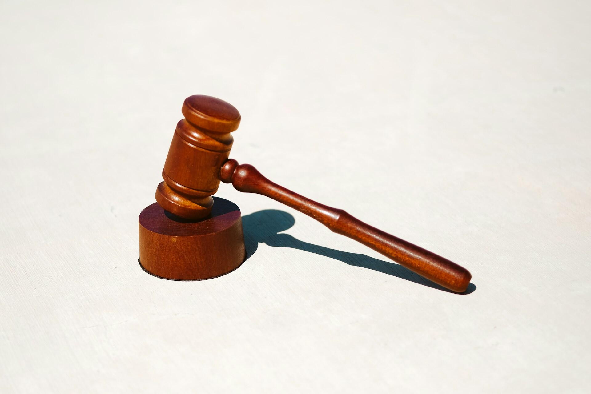 Wooden judge's gavel resting on its circular sound block on a light surface, casting a shadow.