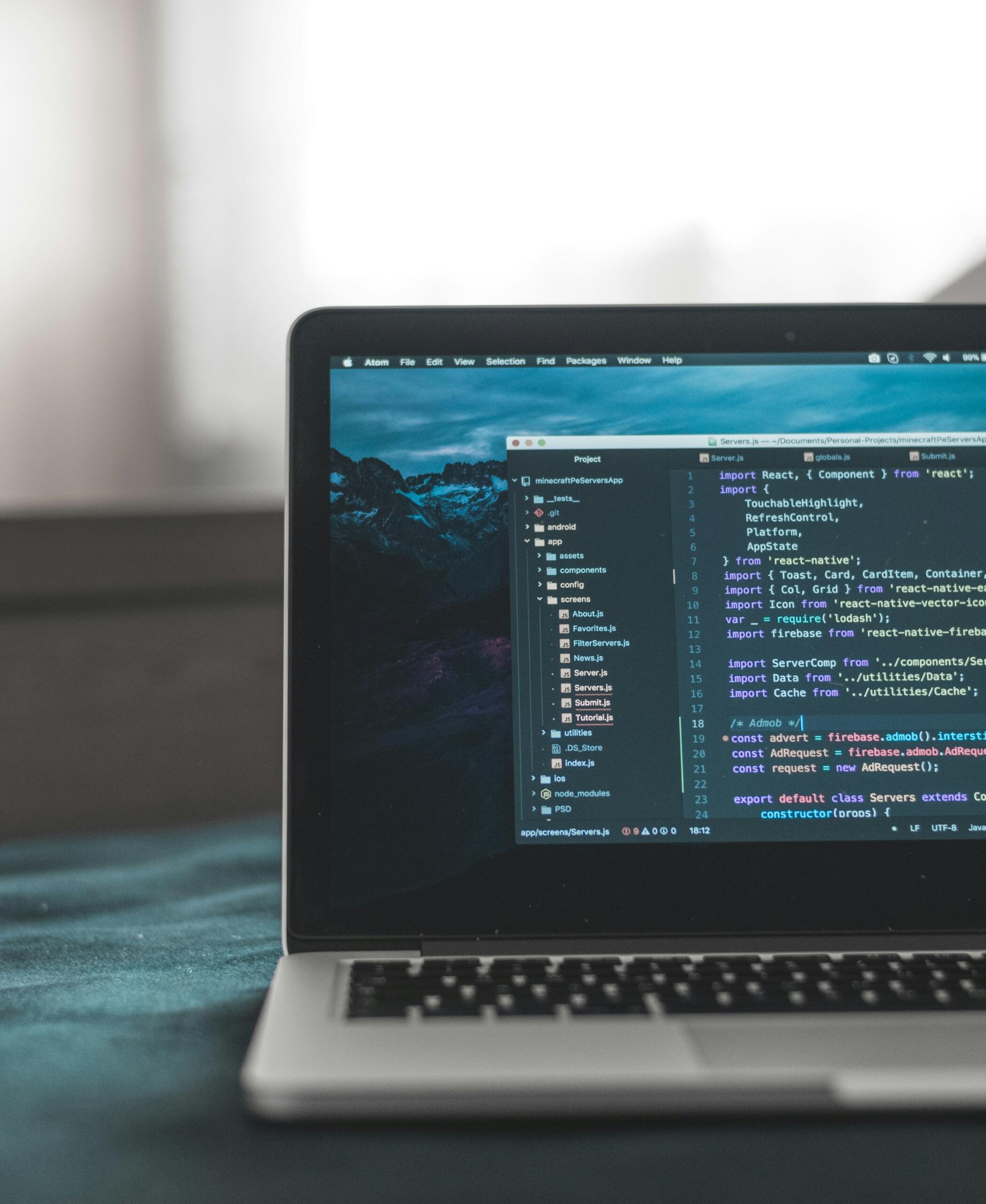Laptop displaying code editor with React.js project files and JavaScript code, set against a blurred background.