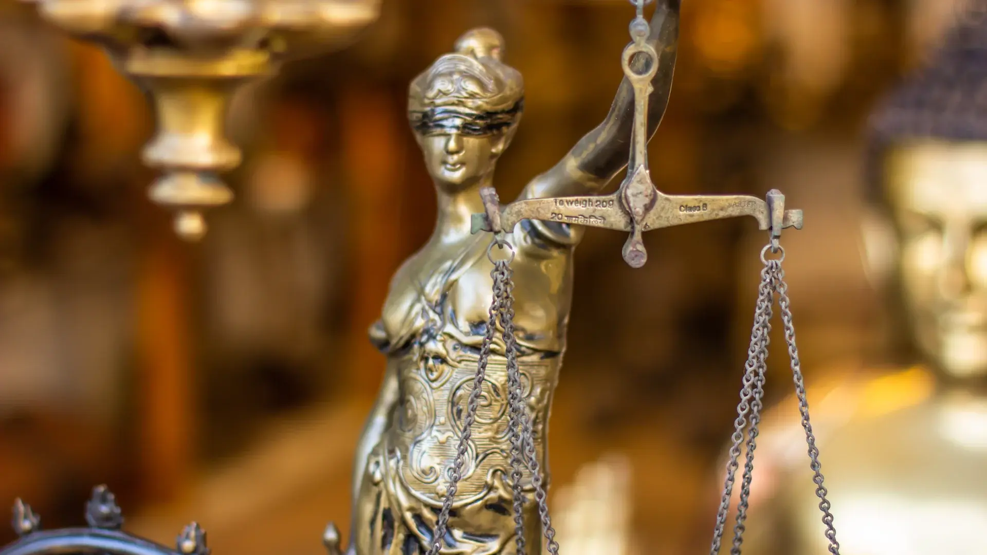 Close-up of a detailed brass Lady Justice statue holding balanced scales, with a blurred golden background.