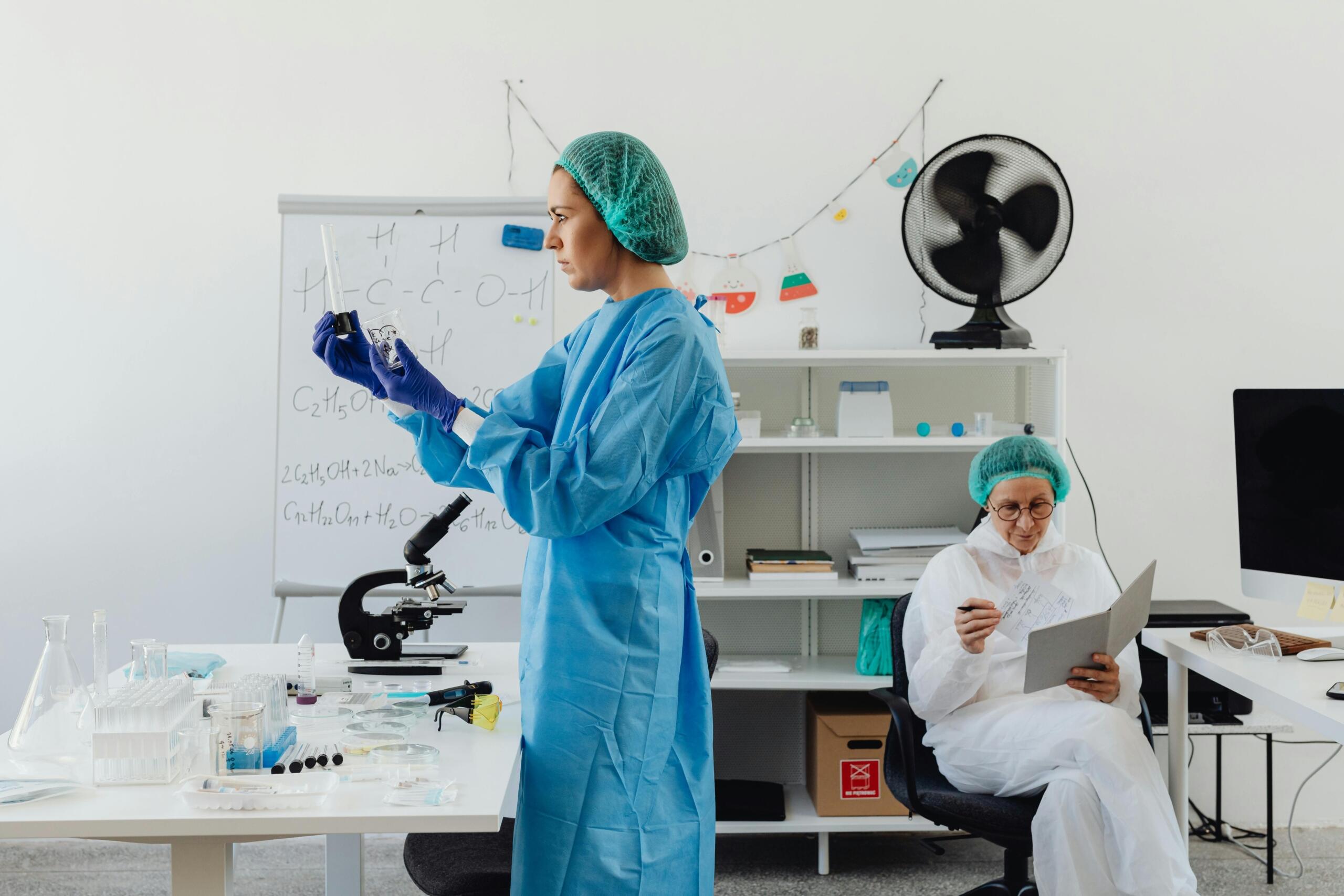 A woman wearing a hair net and laboratory coat works carefully in a scientific laboratory. She appears to be monitoring equipment or conducting an experiment, highlighting the role of physics in research, precision measurement, materials science, and the development of new technologies.