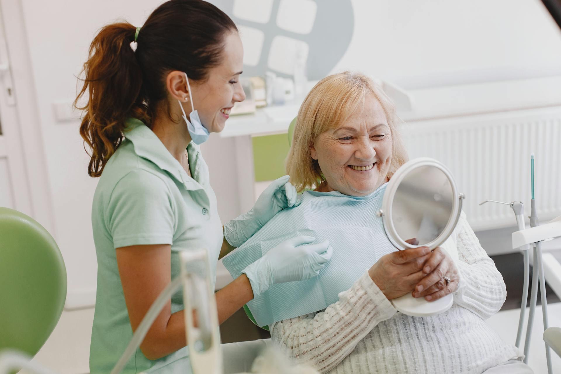 a dentist smiles along with their patient who is looking at their teeth in a mirror