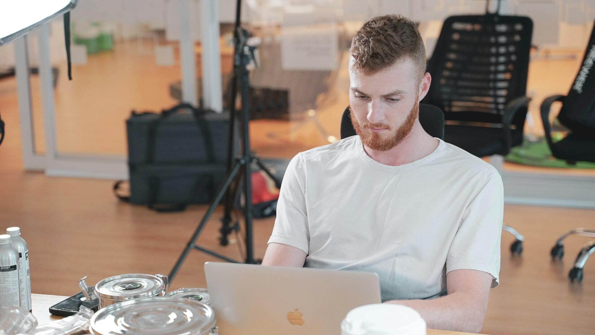 A person sitting in an office chair working on a laptop, with office equipment and chairs in the background.