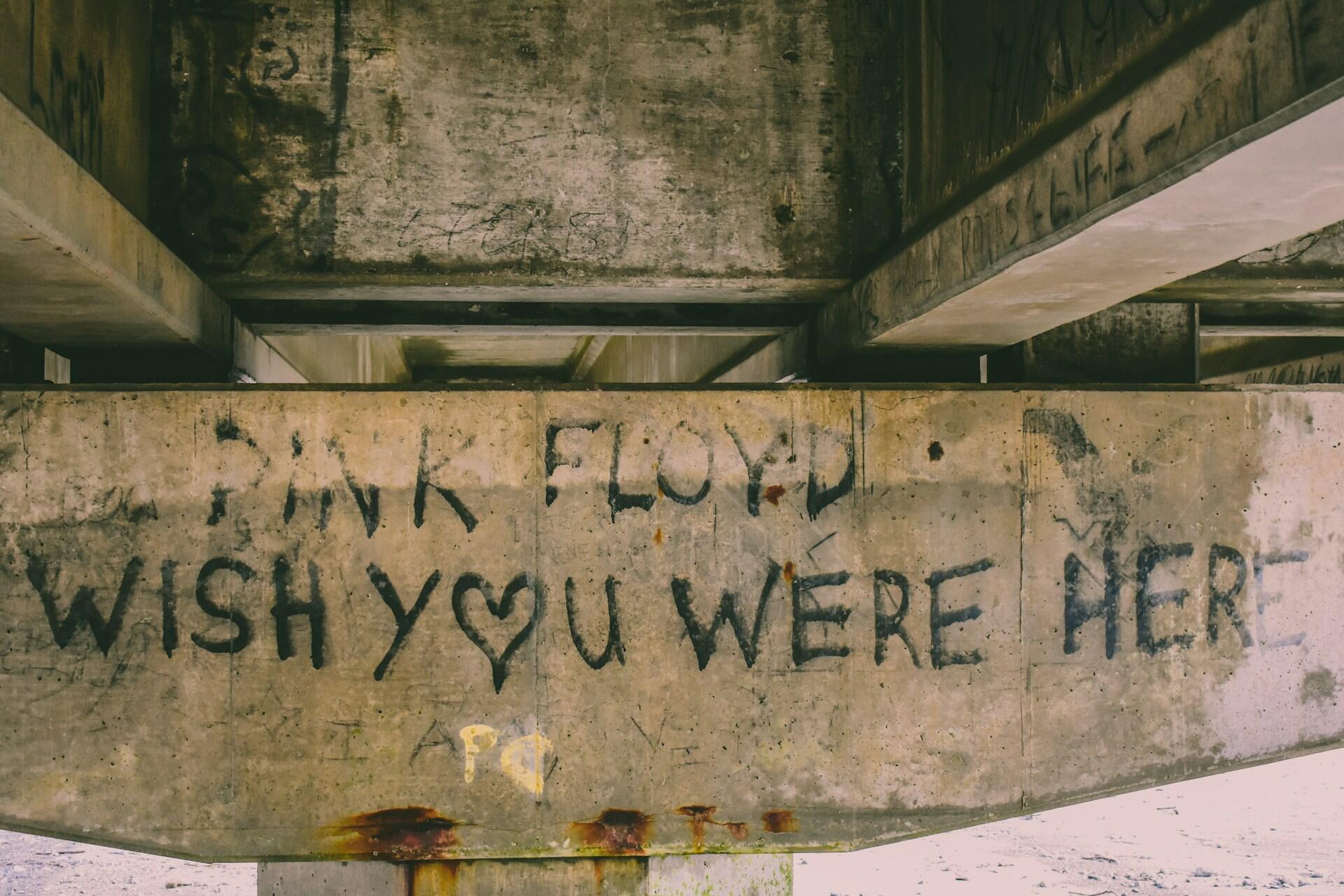 Graffiti on a concrete wall under a bridge reads 