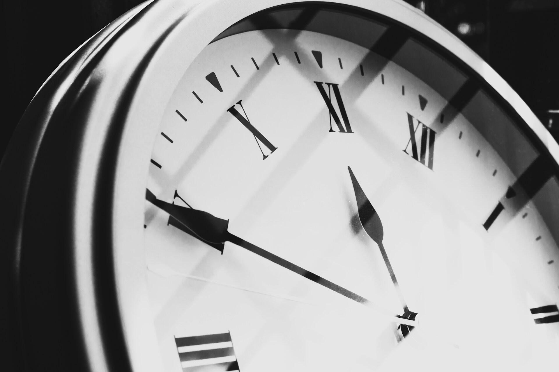 Close-up of a round clock face with Roman numerals showing the time at 11:49 with shadows cast over it.