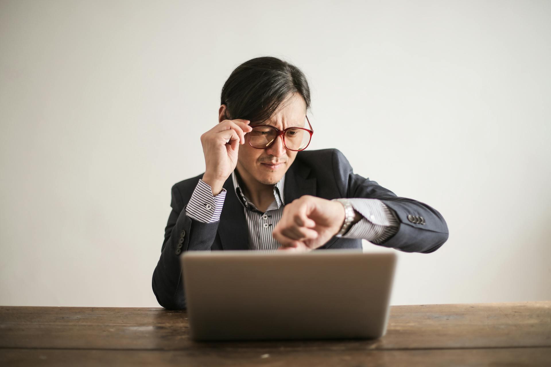 A woman in a suit and glasses is focused on her laptop, engaged in work or research.