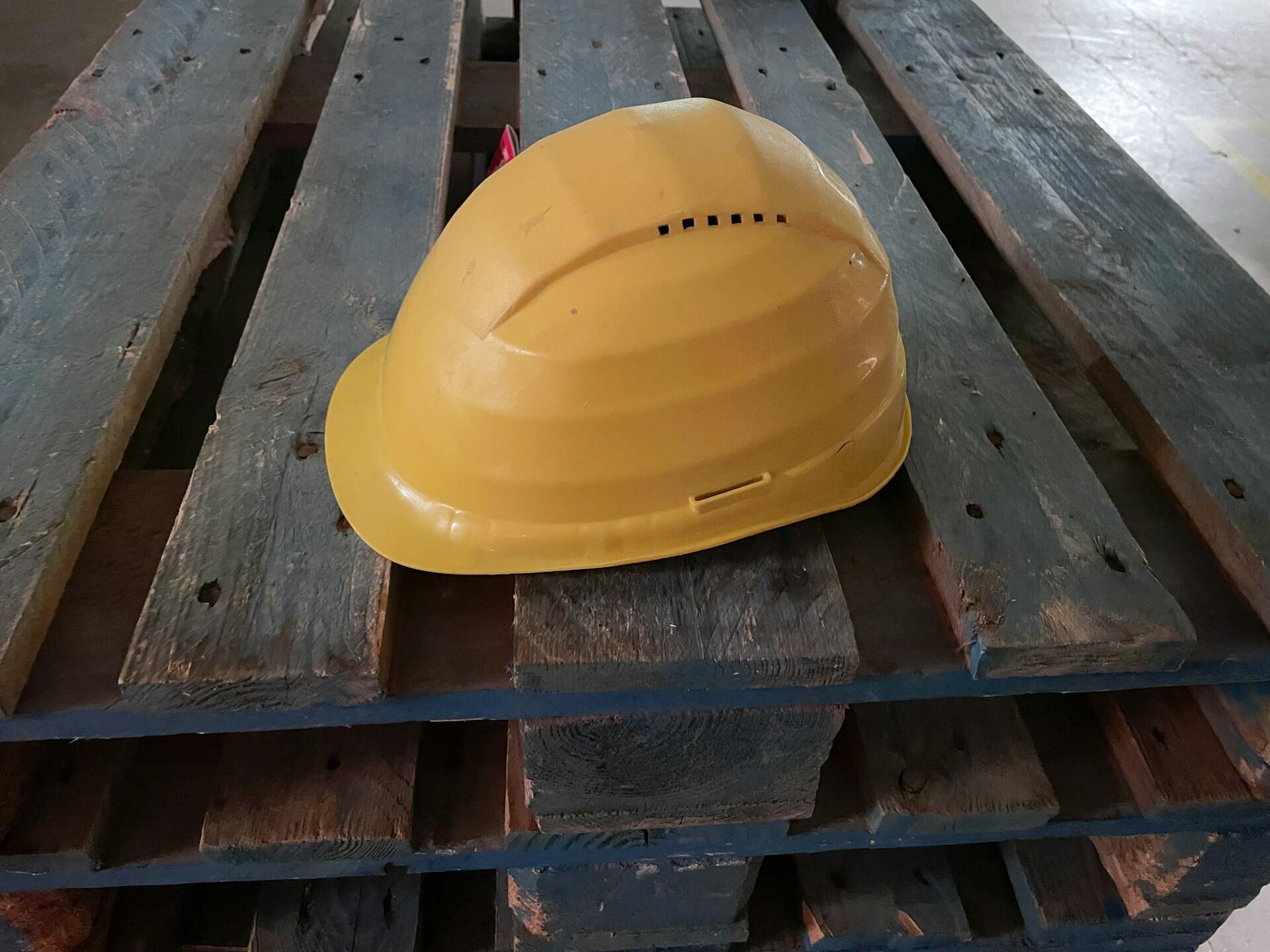 Yellow construction hard hat placed on top of stacked weathered wooden pallets in a warehouse.