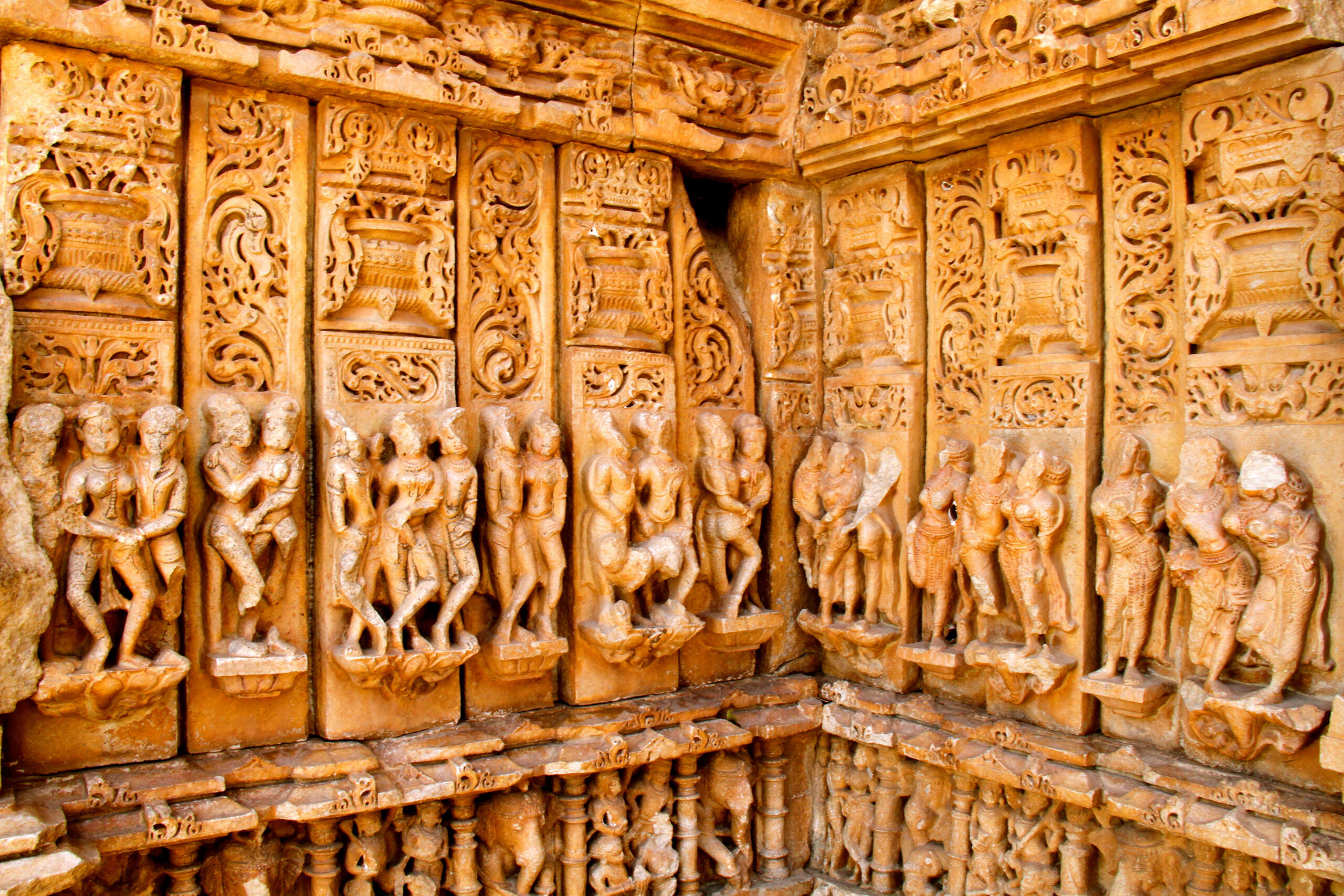 Intricately carved sandstone reliefs depicting figures and decorative motifs on a Hindu temple wall.